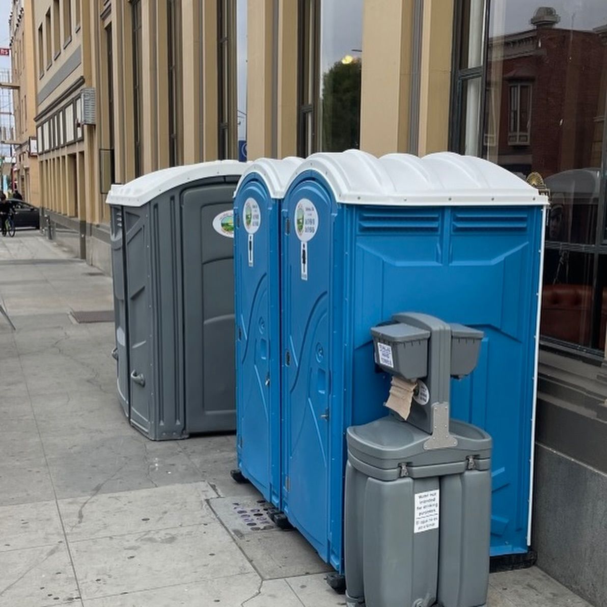 A row of blue and gray portable toilets on a sidewalk