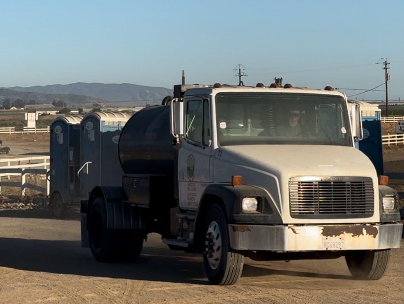 A white truck is parked in a dirt lot with mountains in the background