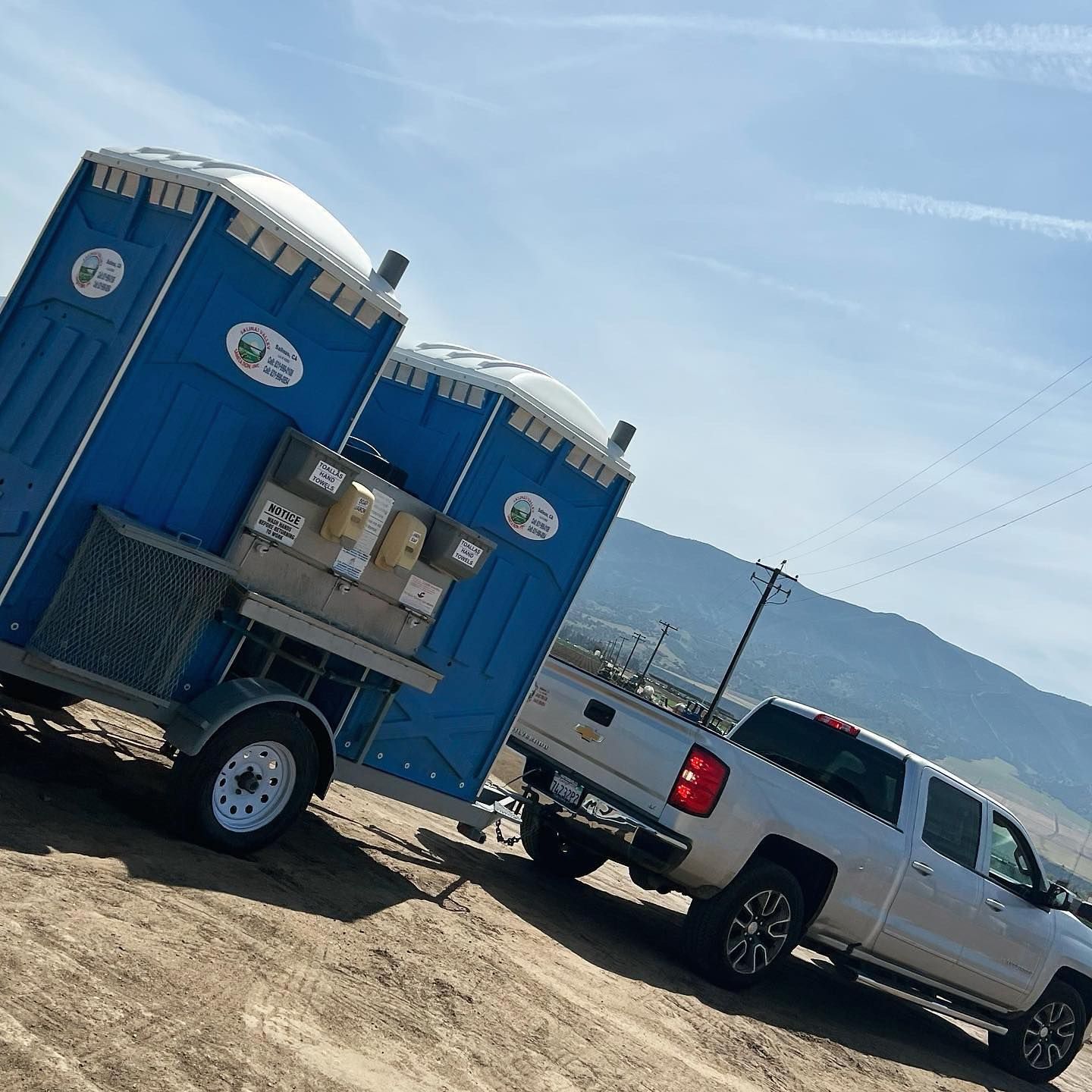 A truck is parked next to two portable toilets on a trailer.