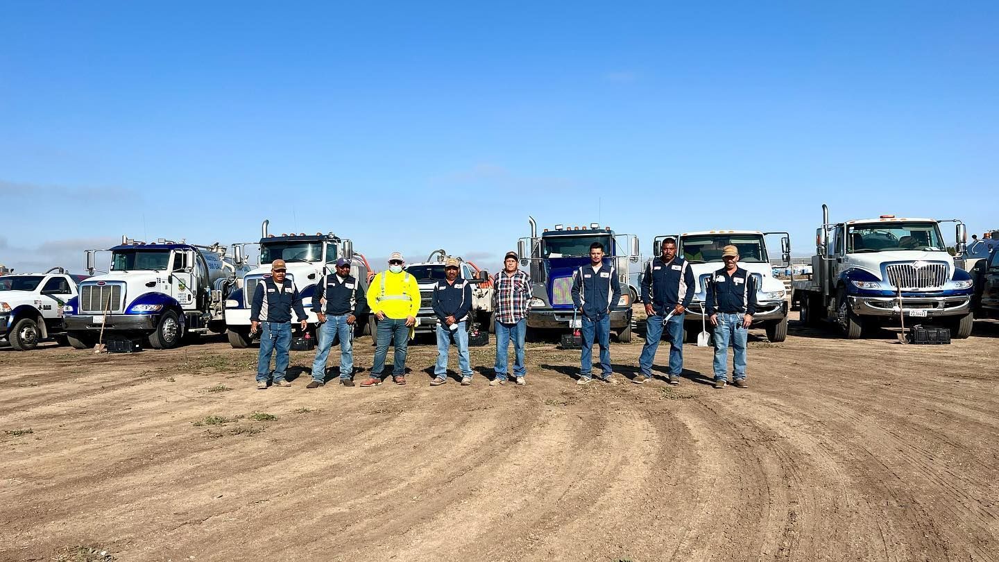 A group of men are standing in front of a row of trucks in a dirt field.
