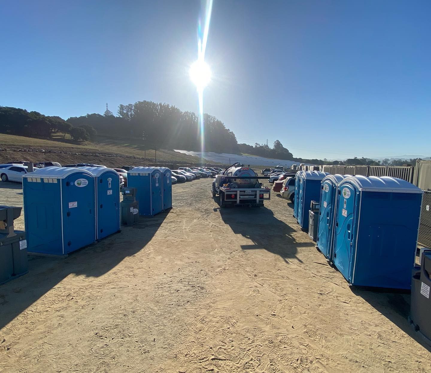 A row of blue portable toilets are lined up in a dirt field.