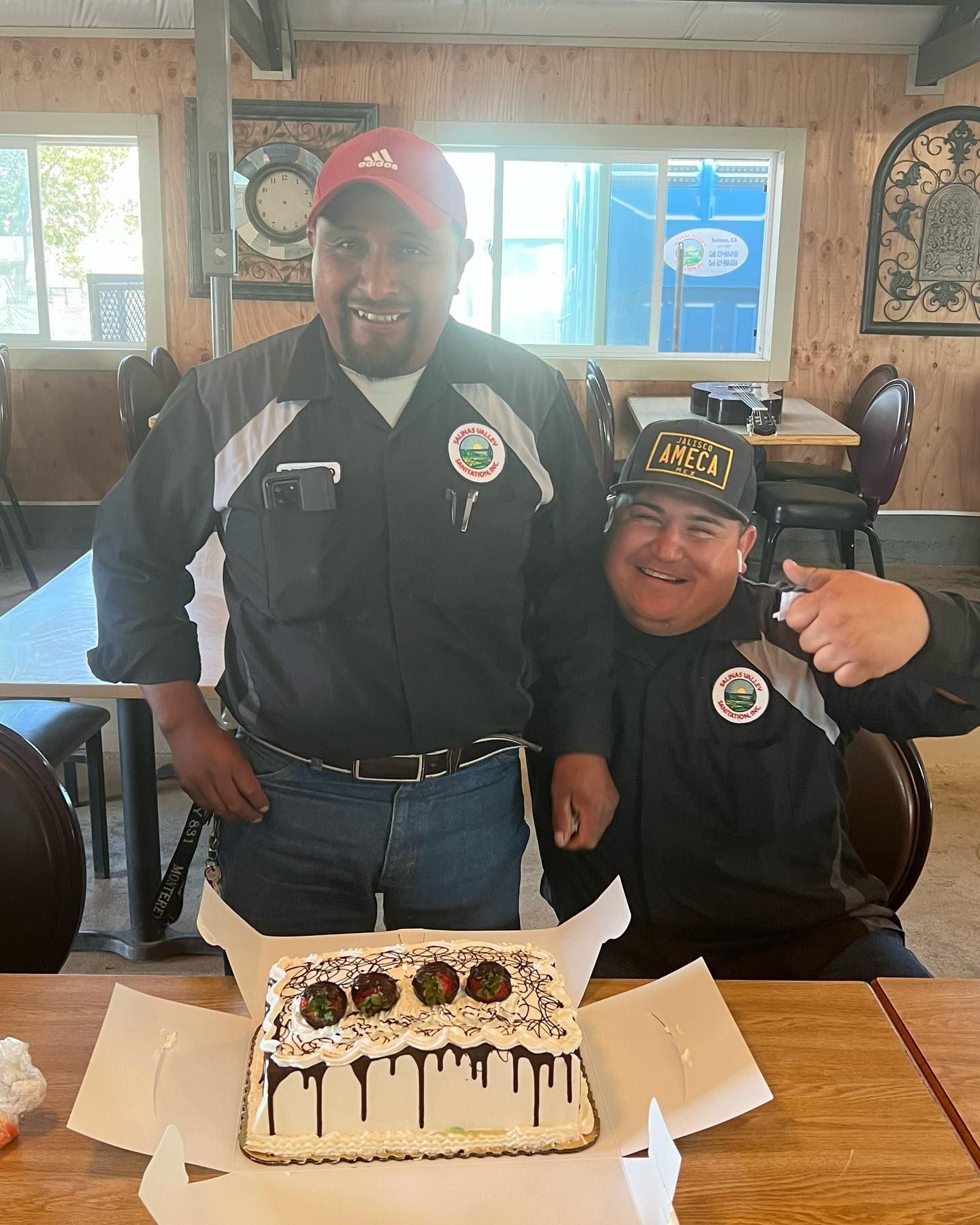 Two men are standing next to a cake on a table.