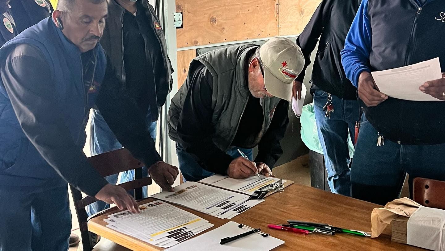 A group of men are standing around a table signing papers.