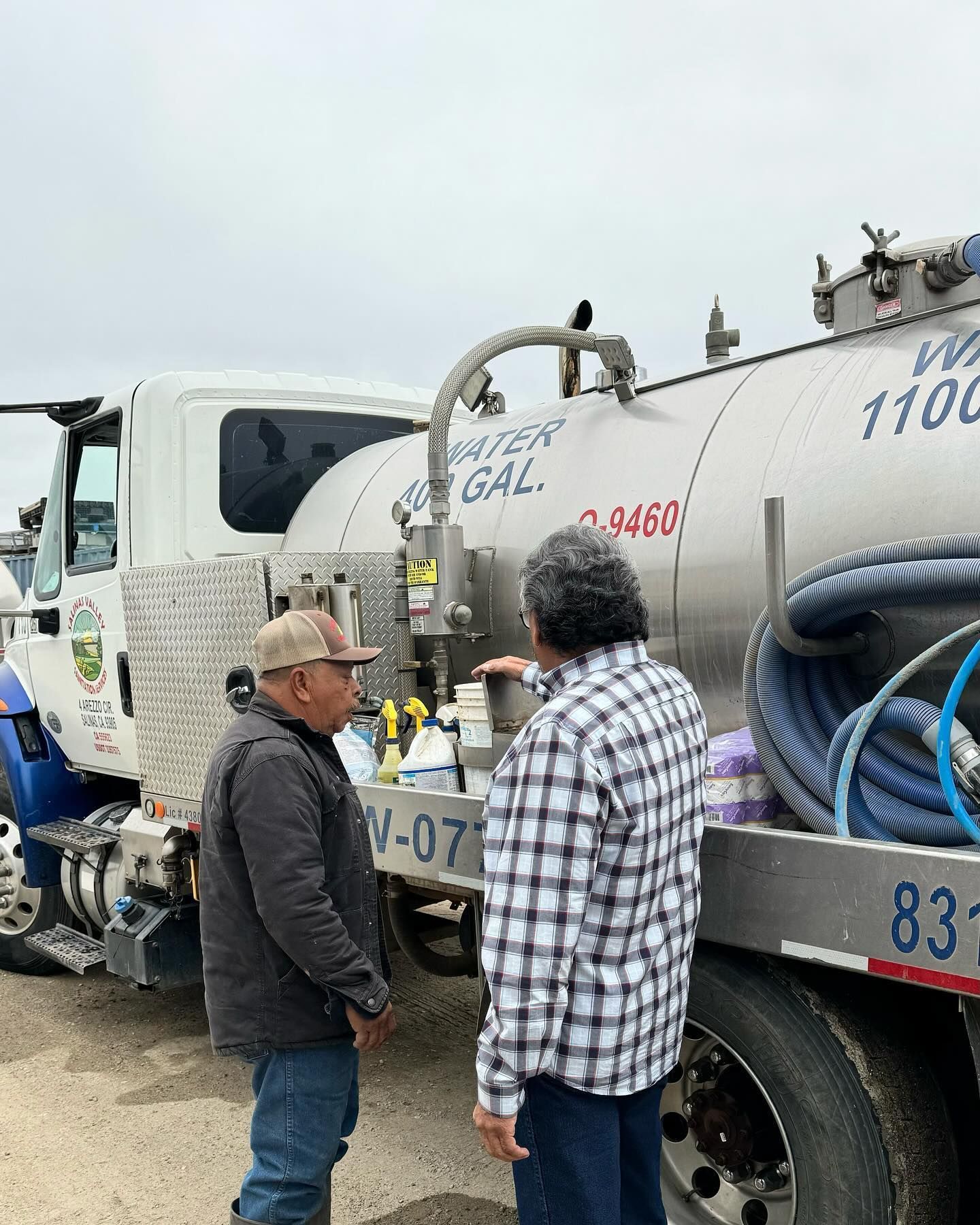 Two men are standing next to a large tanker truck.