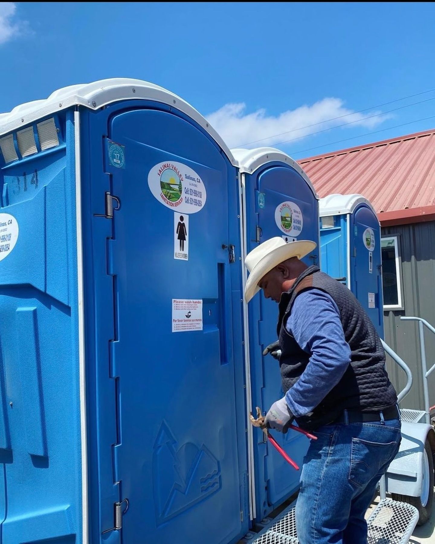 A man in a cowboy hat is working on a portable toilet