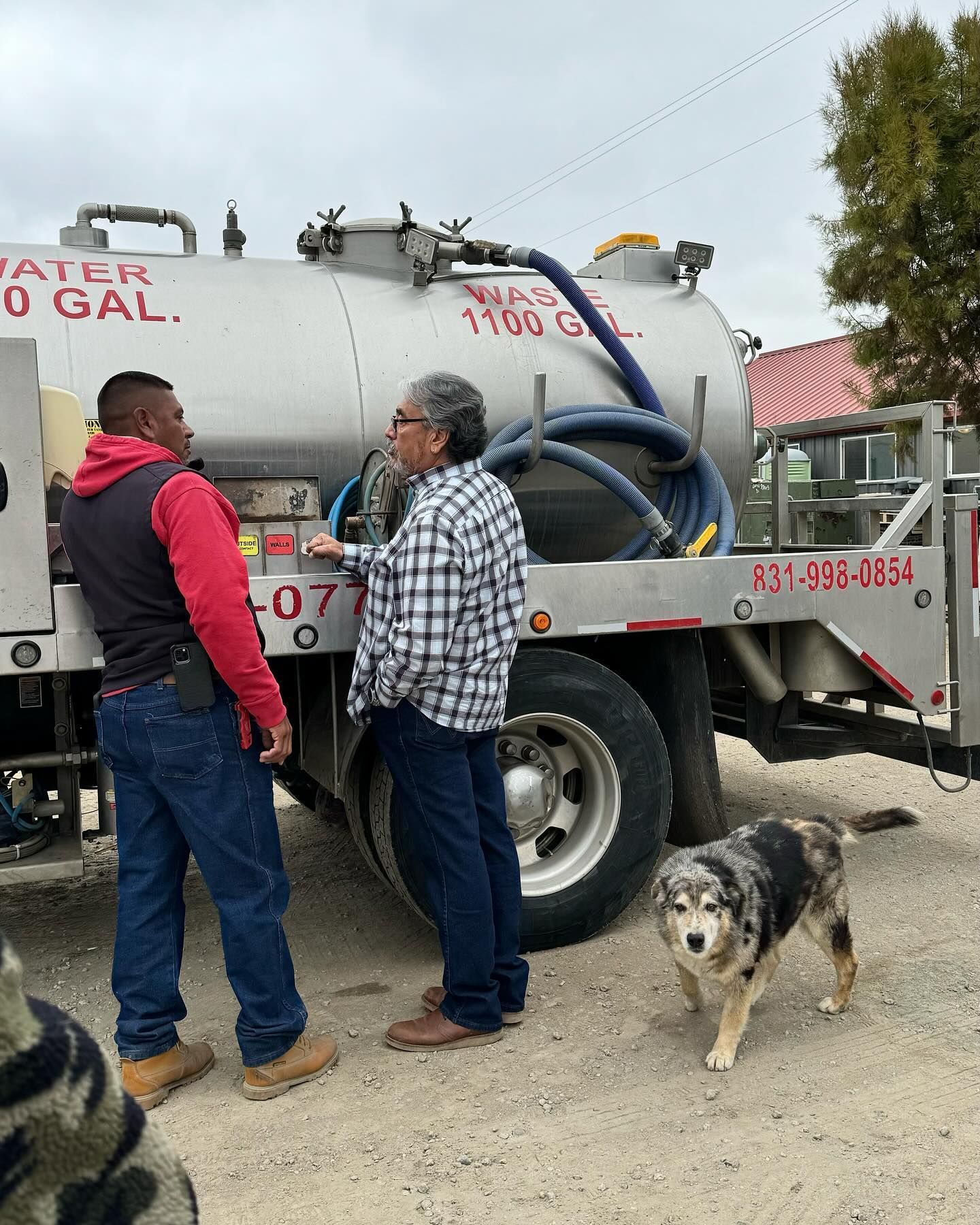 Two men and a dog are standing in front of a vacuum truck.