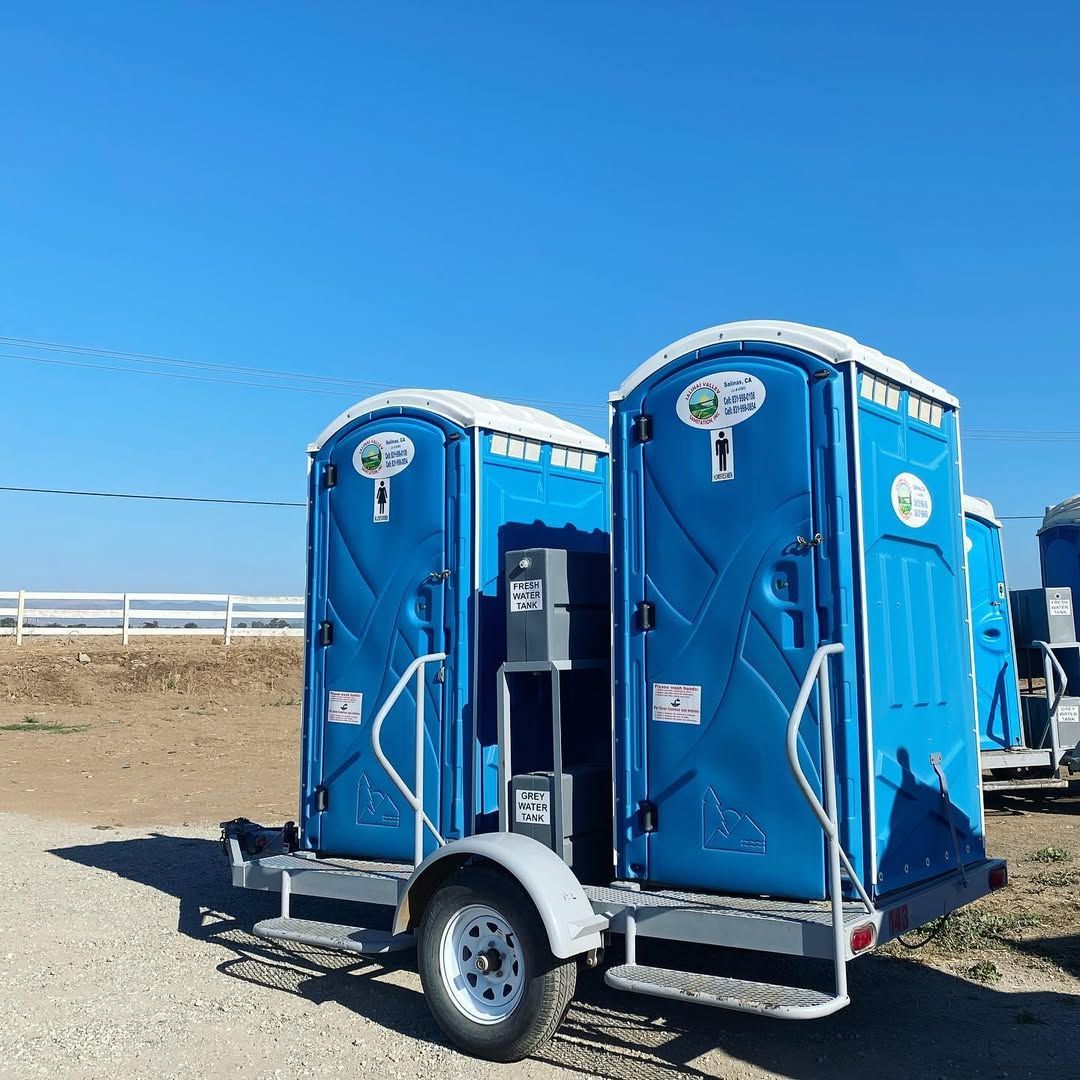 A row of blue portable toilets are lined up on a sidewalk.