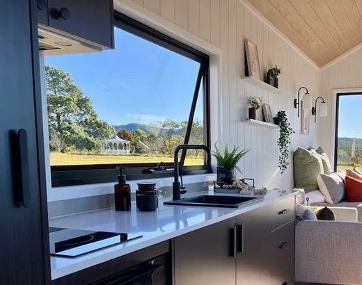 Modern kitchen with open window, overlooking a scenic landscape. Black cabinets, white countertops.