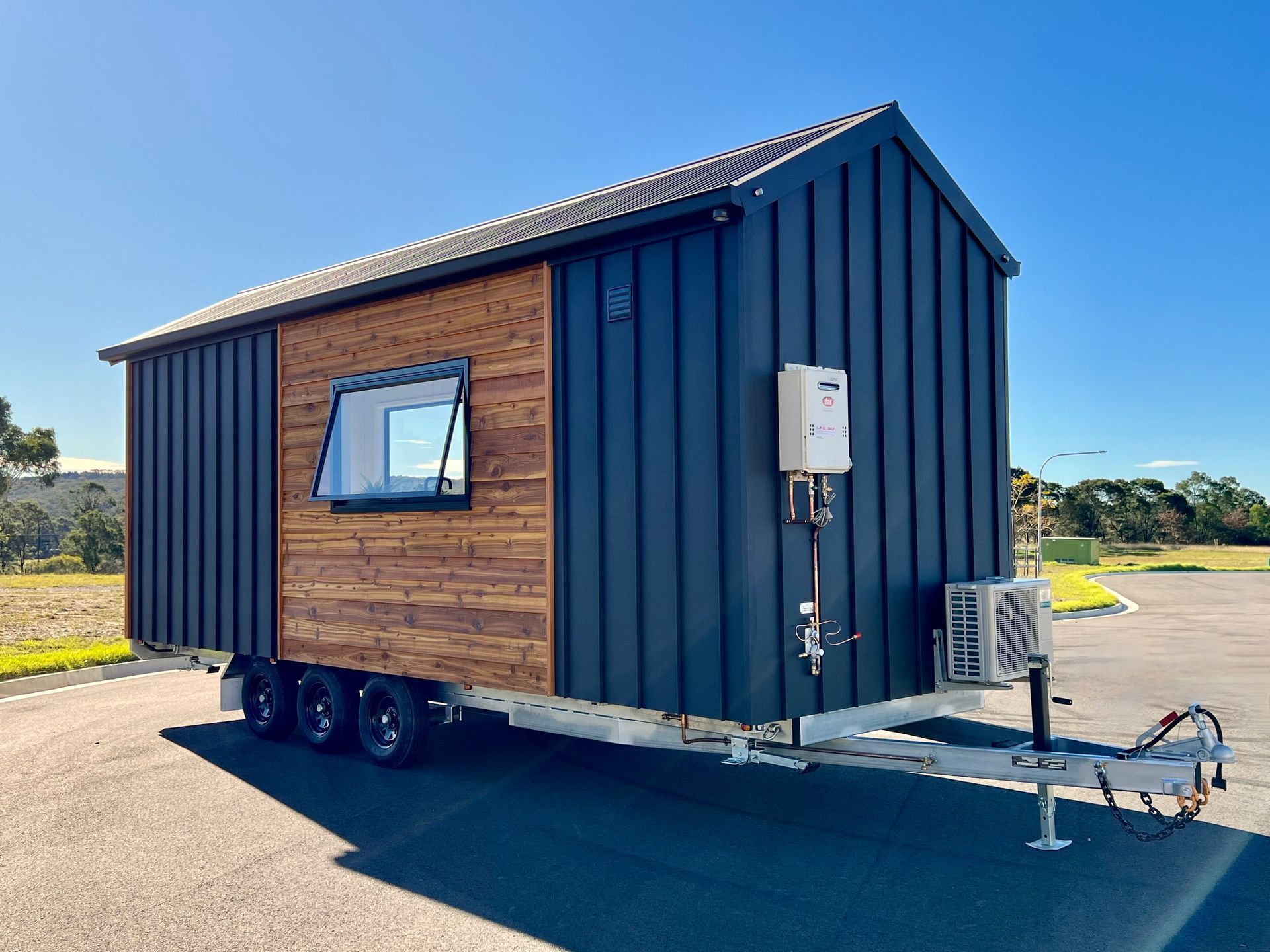 Tiny house on a trailer with black siding, wood accents, and a white electrical box.