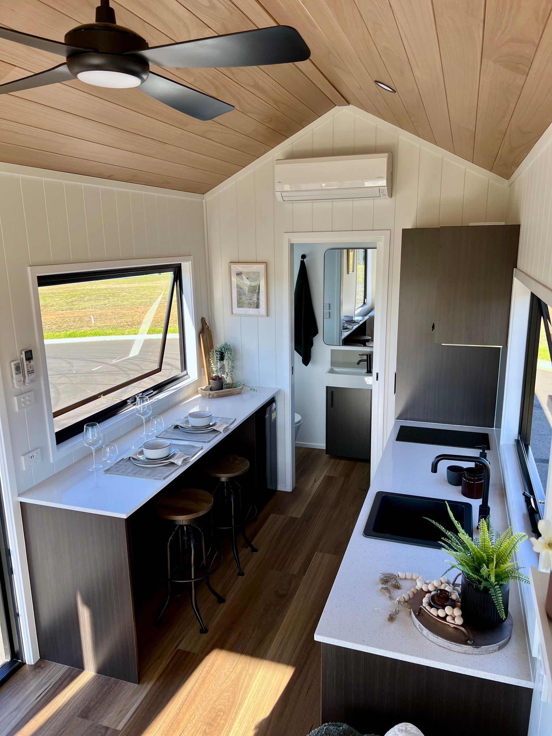 Interior of a tiny home with a kitchen, counter seating, and a bathroom at the end.