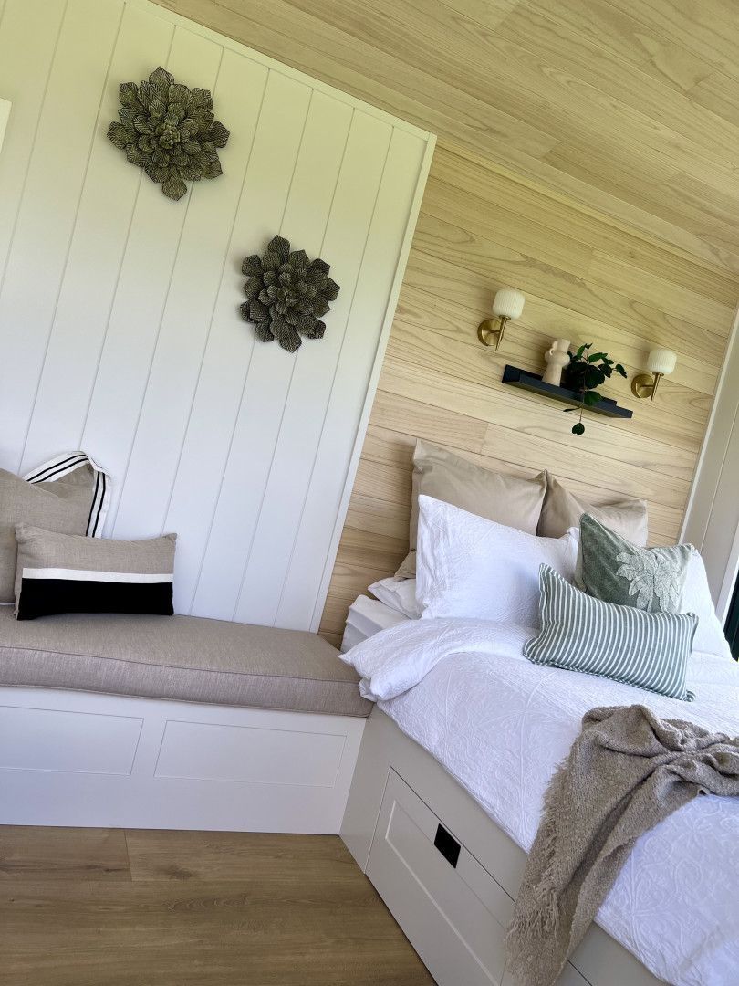 Cozy bedroom with a built-in bench, white bed, light wood walls, and decorative floral accents.
