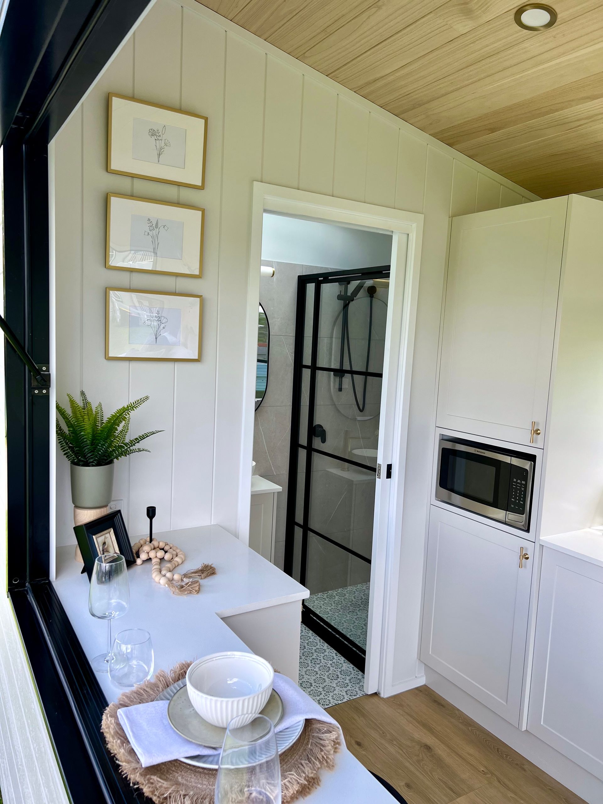 Tiny home interior with a dining nook, open door to bathroom, and white cabinetry.