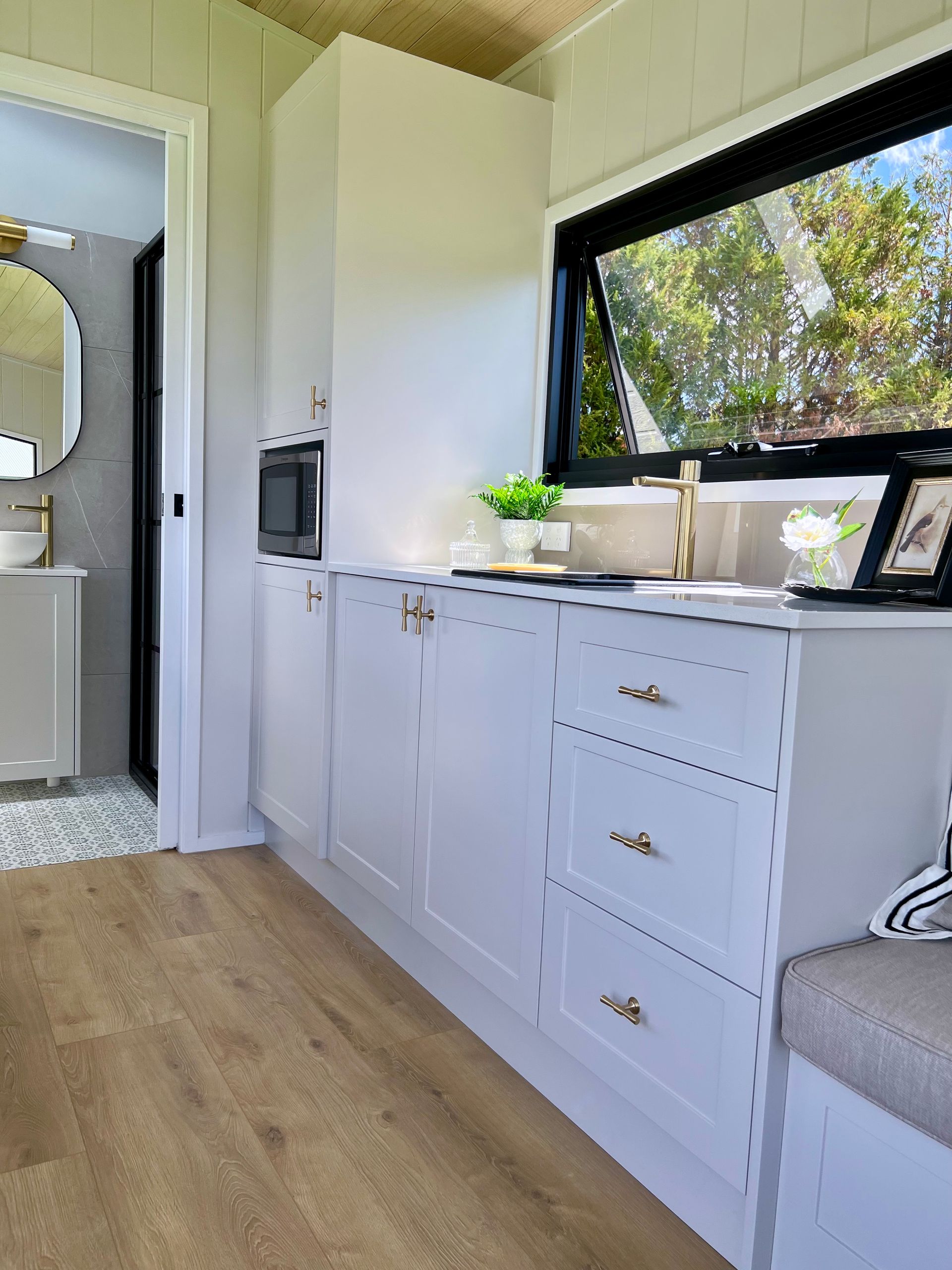 White kitchen cabinets in a small home with a microwave, window, and an open doorway to a bathroom.