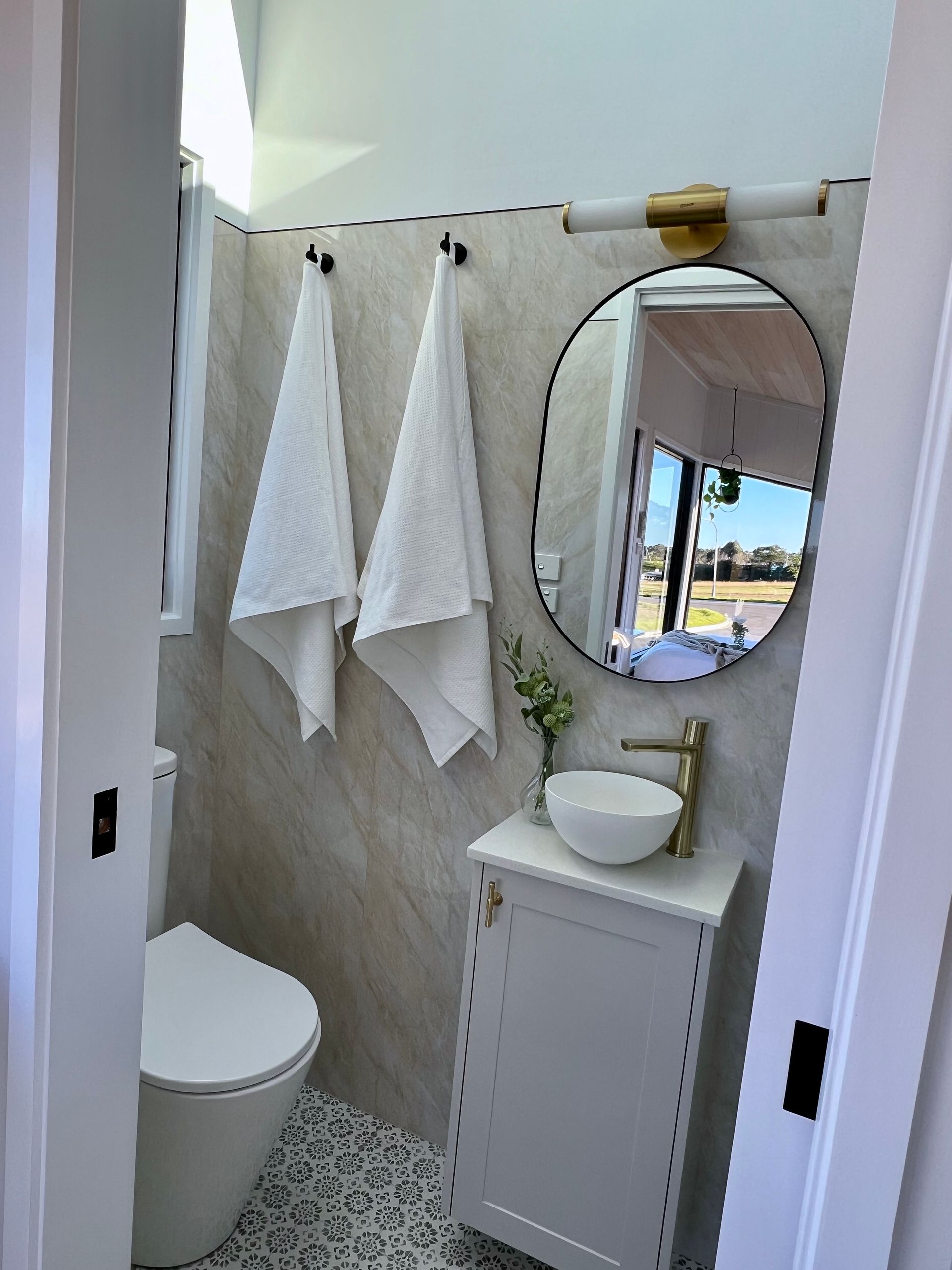 Small, modern bathroom with white fixtures, light tan tile, and gold accents.
