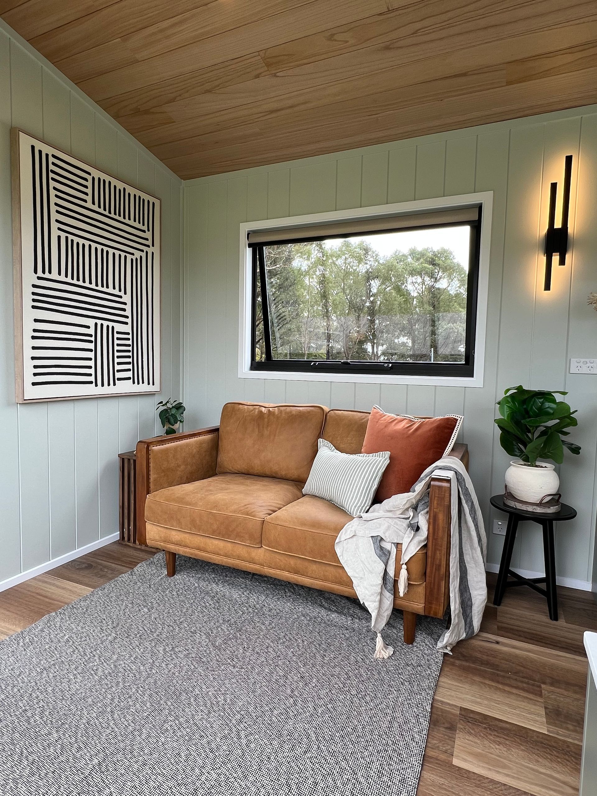 Cozy living room with brown sofa, abstract art, zebra rug, and a window overlooking trees.
