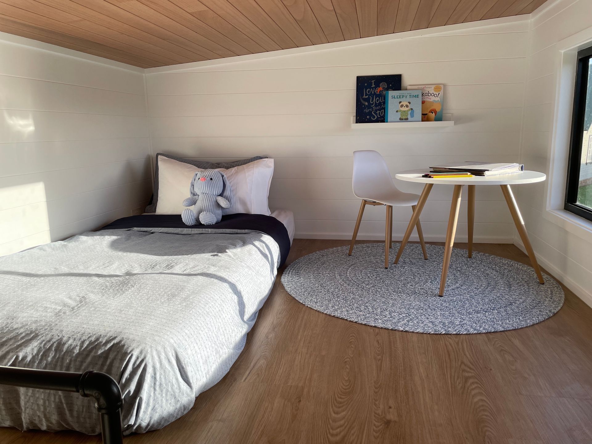 Small bedroom with bed, desk, and rug; white walls, wooden ceiling, and floor.