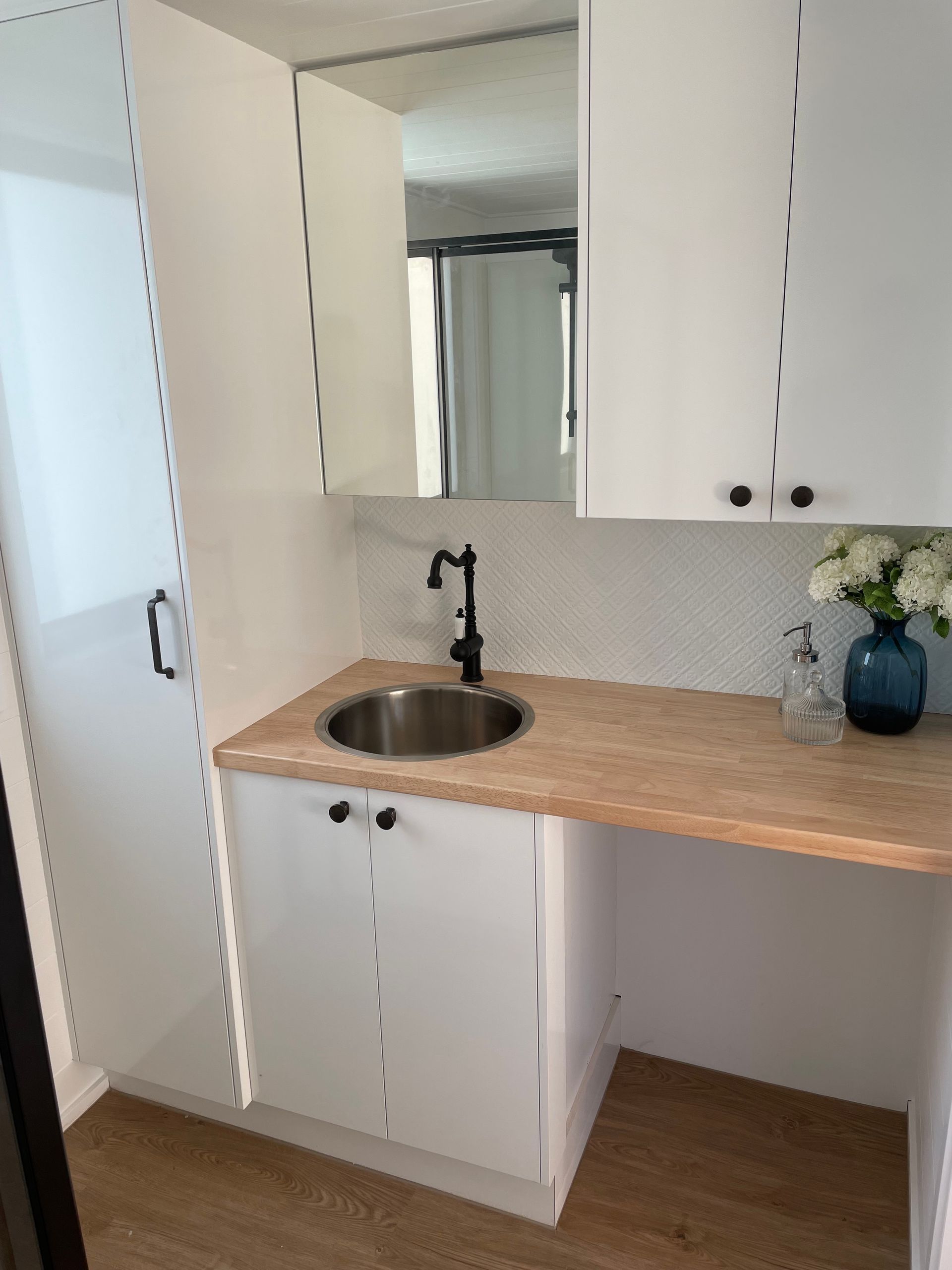Small bathroom with a sink, white cabinets, and a light wood countertop.