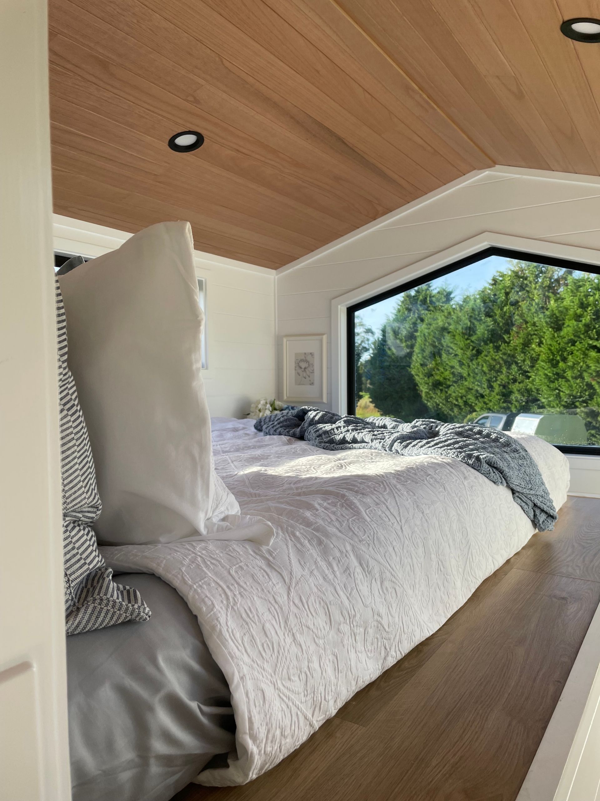 Cozy bedroom with wood ceiling, white bed, large window overlooking greenery.