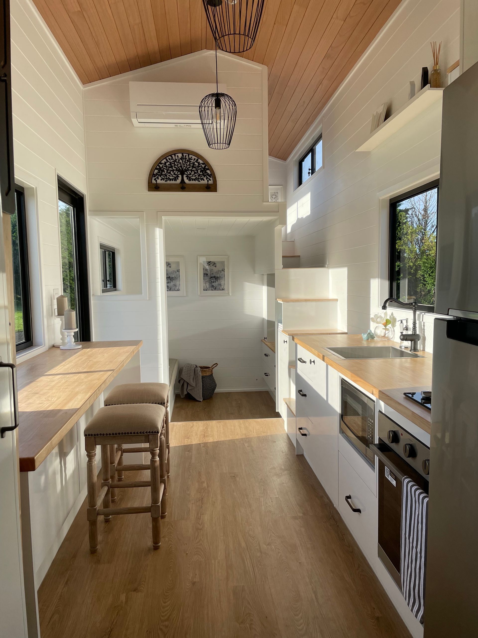 Cozy tiny home interior with wood accents and white walls. Includes kitchen, dining area, and loft.