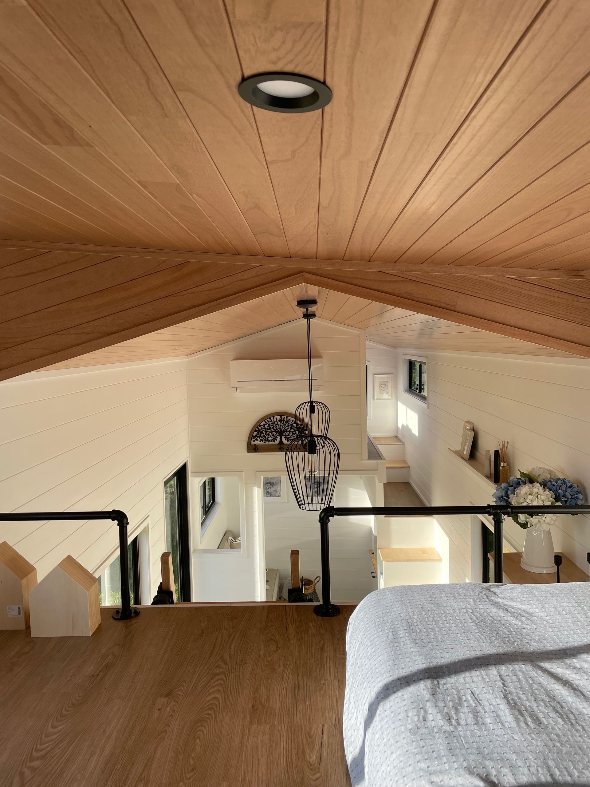 Interior view of a tiny home loft with wooden ceiling and walls, overlooking a living space.