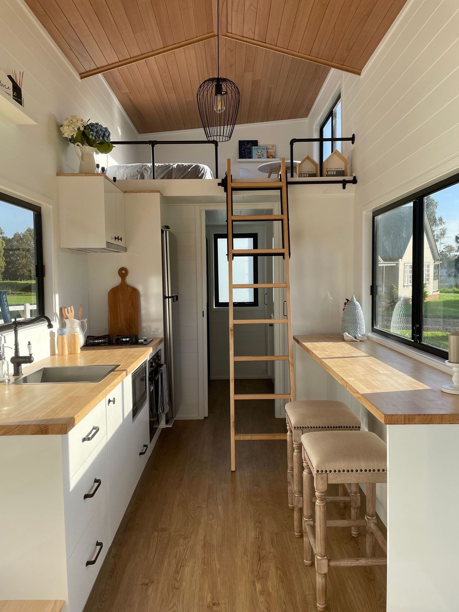 Cozy tiny home interior. Kitchen with wood counters, a loft with ladder, and bar seating.
