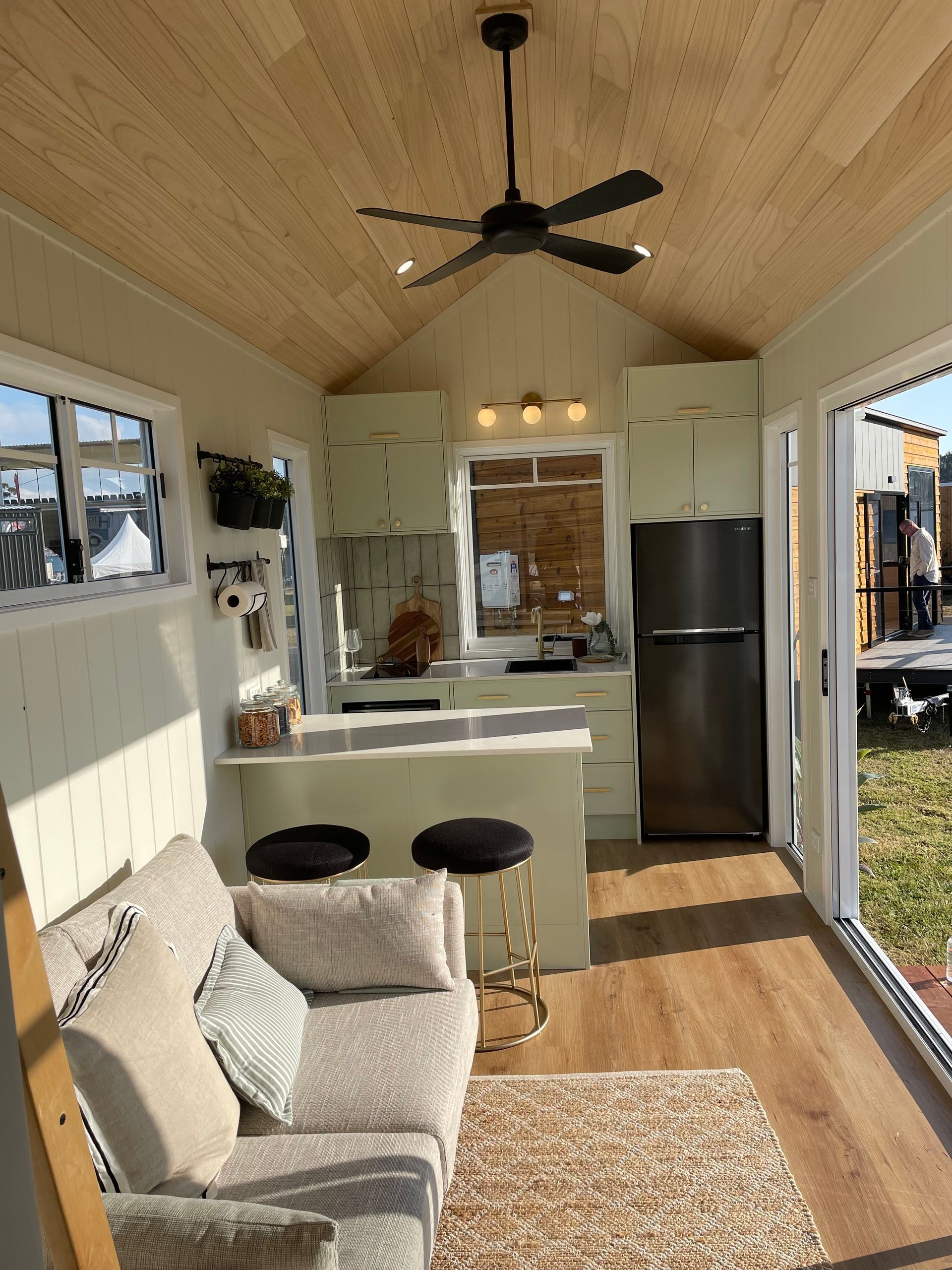 Cozy tiny home interior with a kitchen, seating area, and sliding glass doors to the outside.