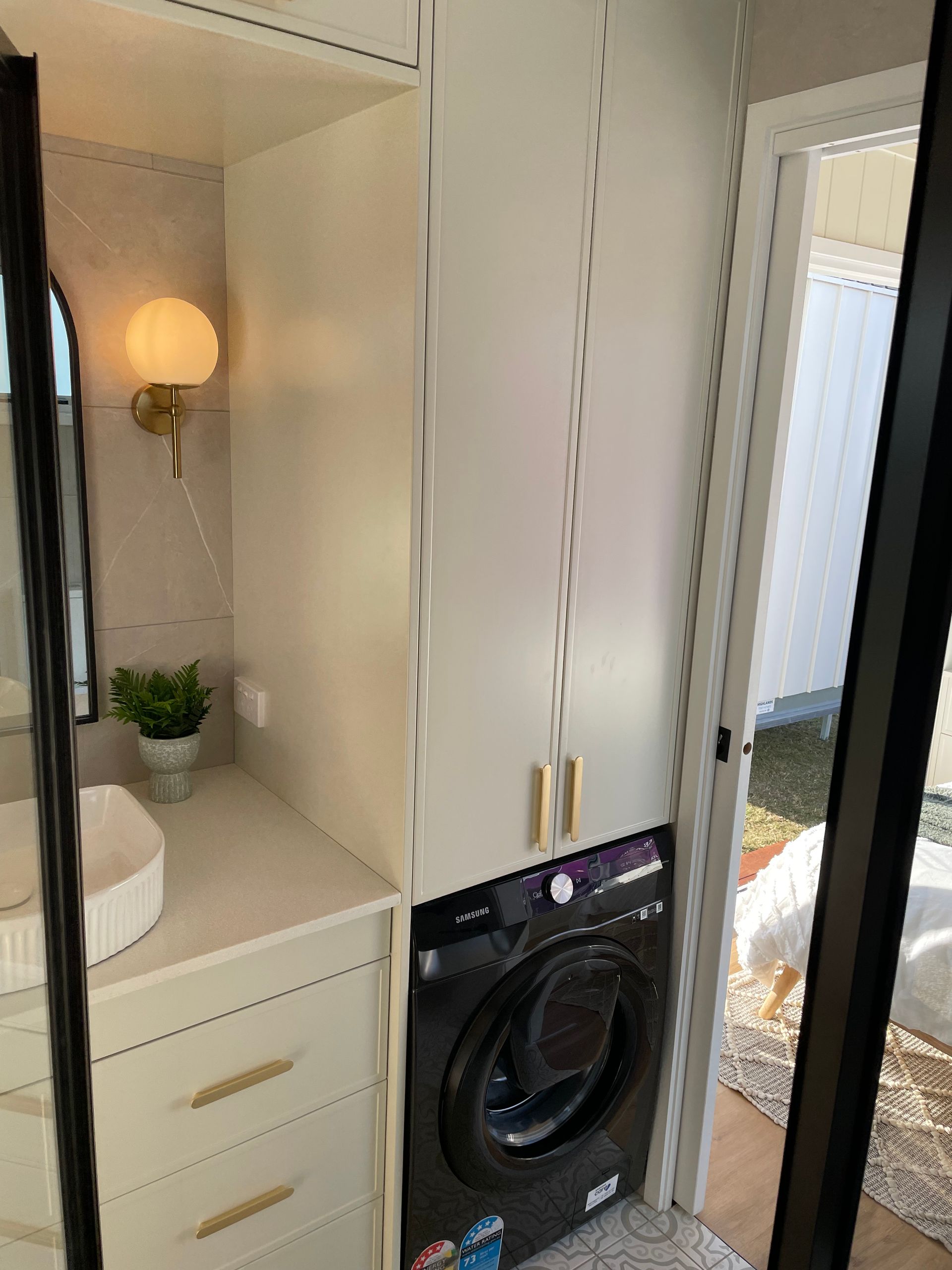 Laundry room with a washer, cabinets, sink, and mirror. Black washer and gold hardware.