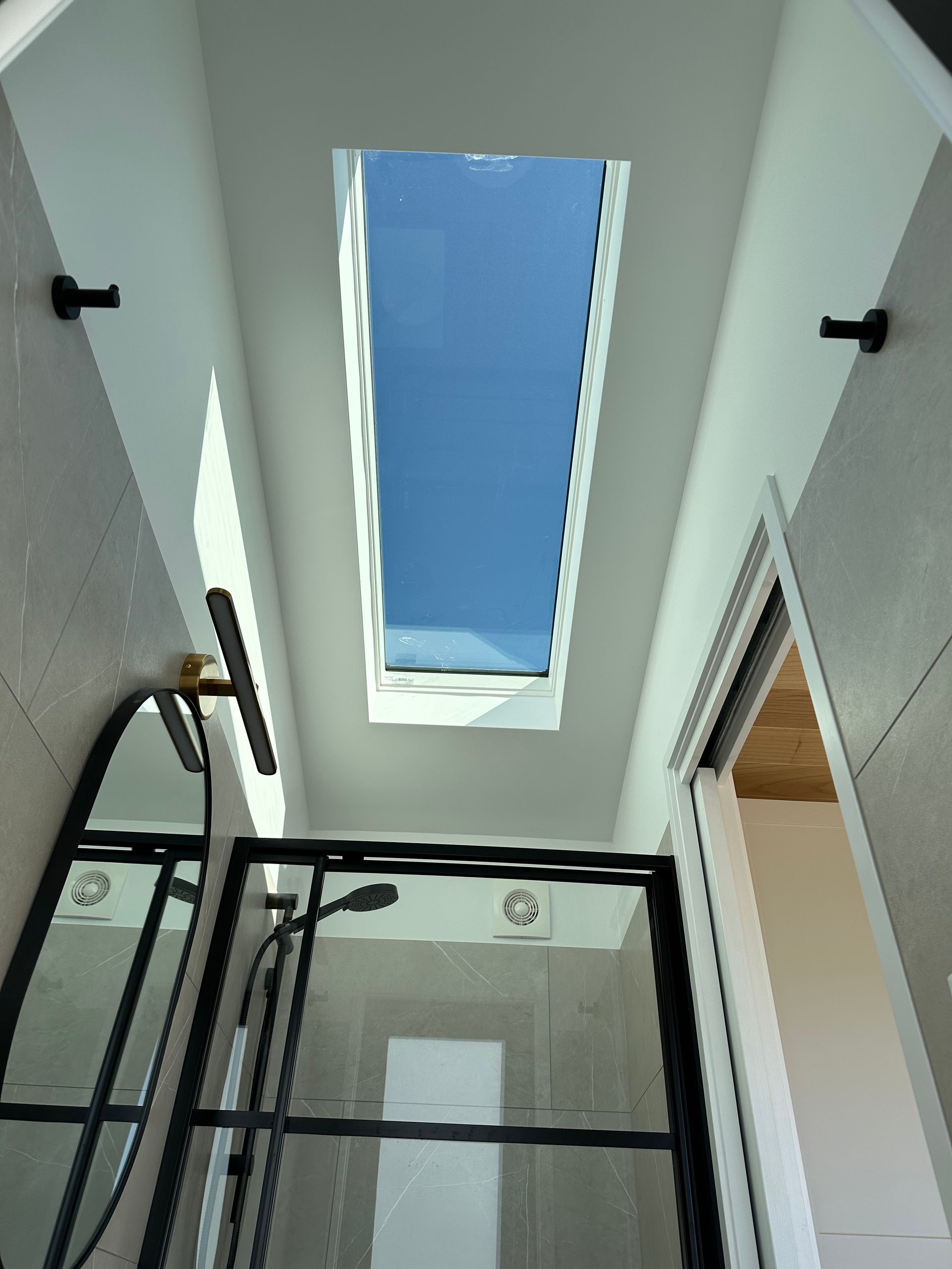 Bathroom with rectangular skylight, glass shower, and black fixtures. Blue sky visible.