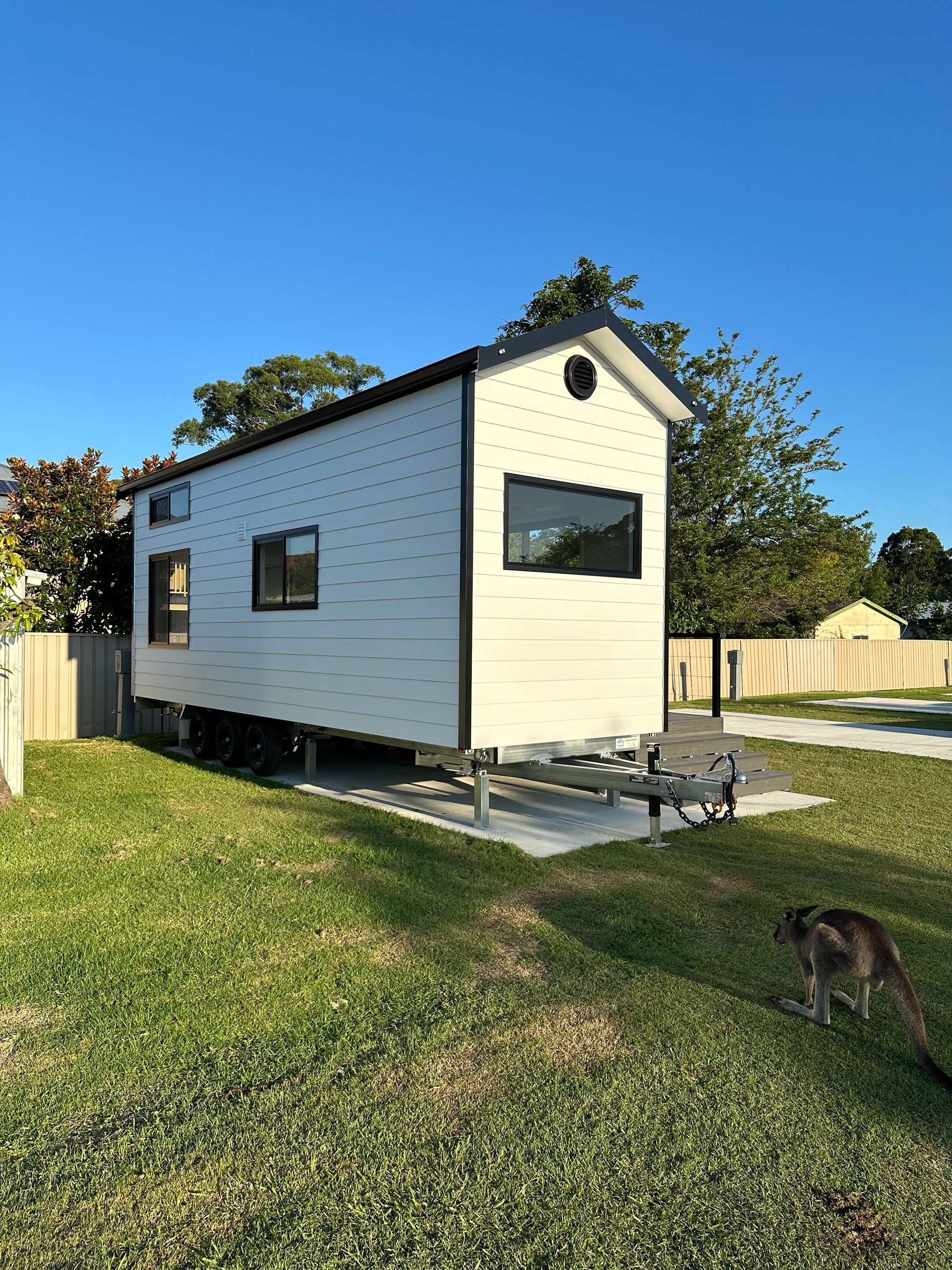 Loft area in a tiny home with wood ceiling, hardwood floor, small window, and a wooden ladder.
