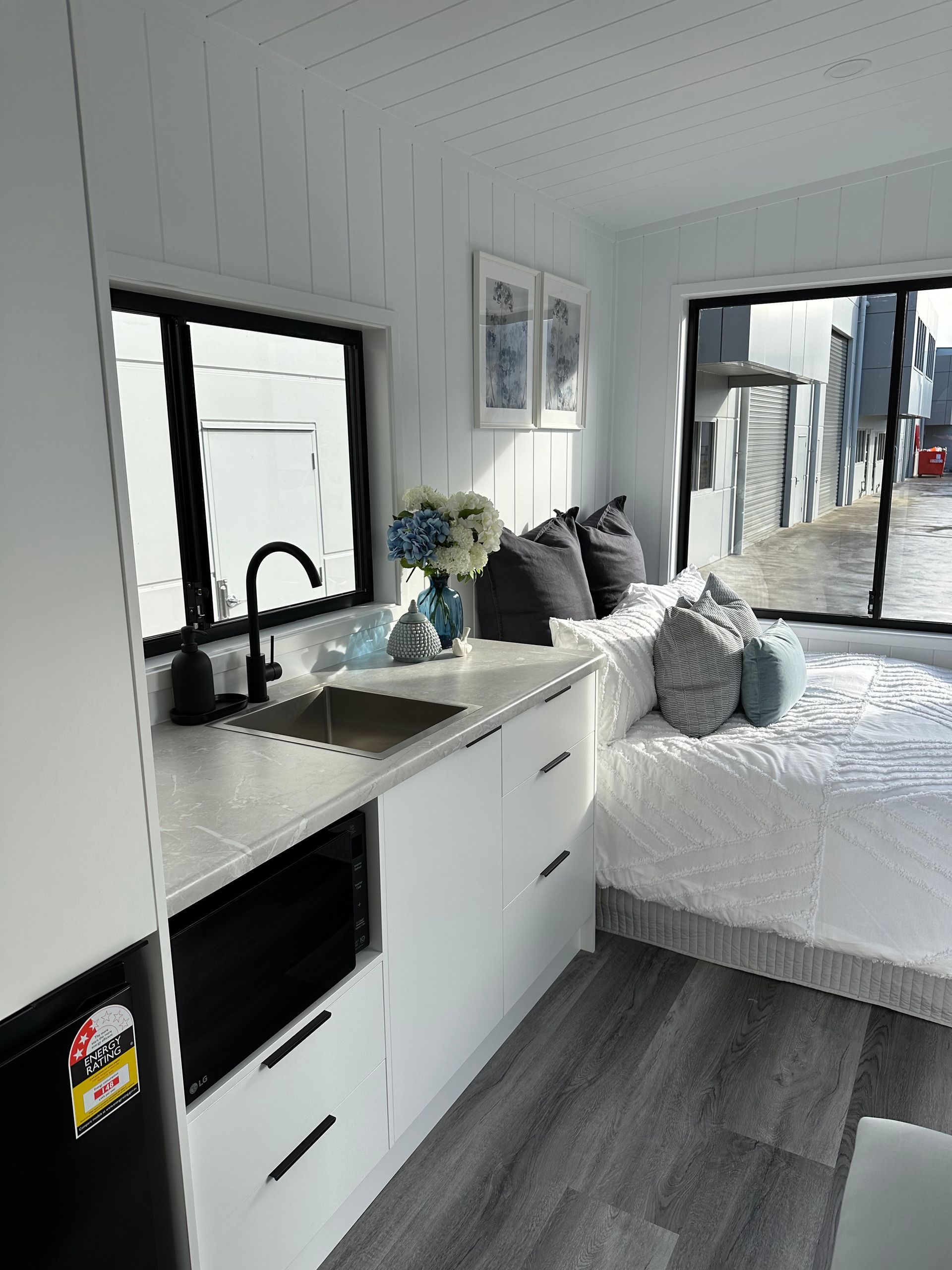 Small, white studio apartment with kitchenette, bed, and large windows.