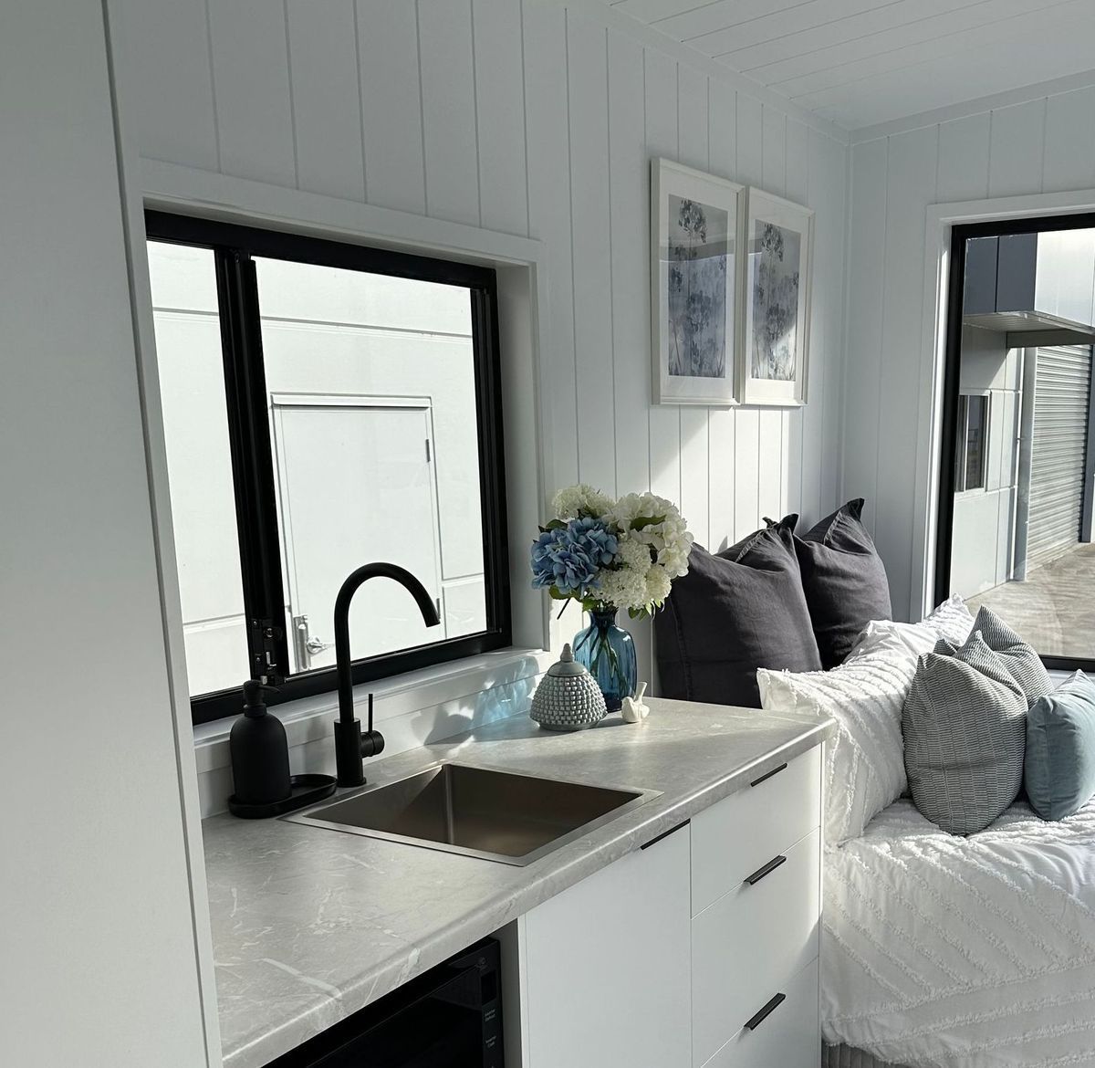 Small kitchen with sink, window, white cabinets, blue and white decor, sunlight.