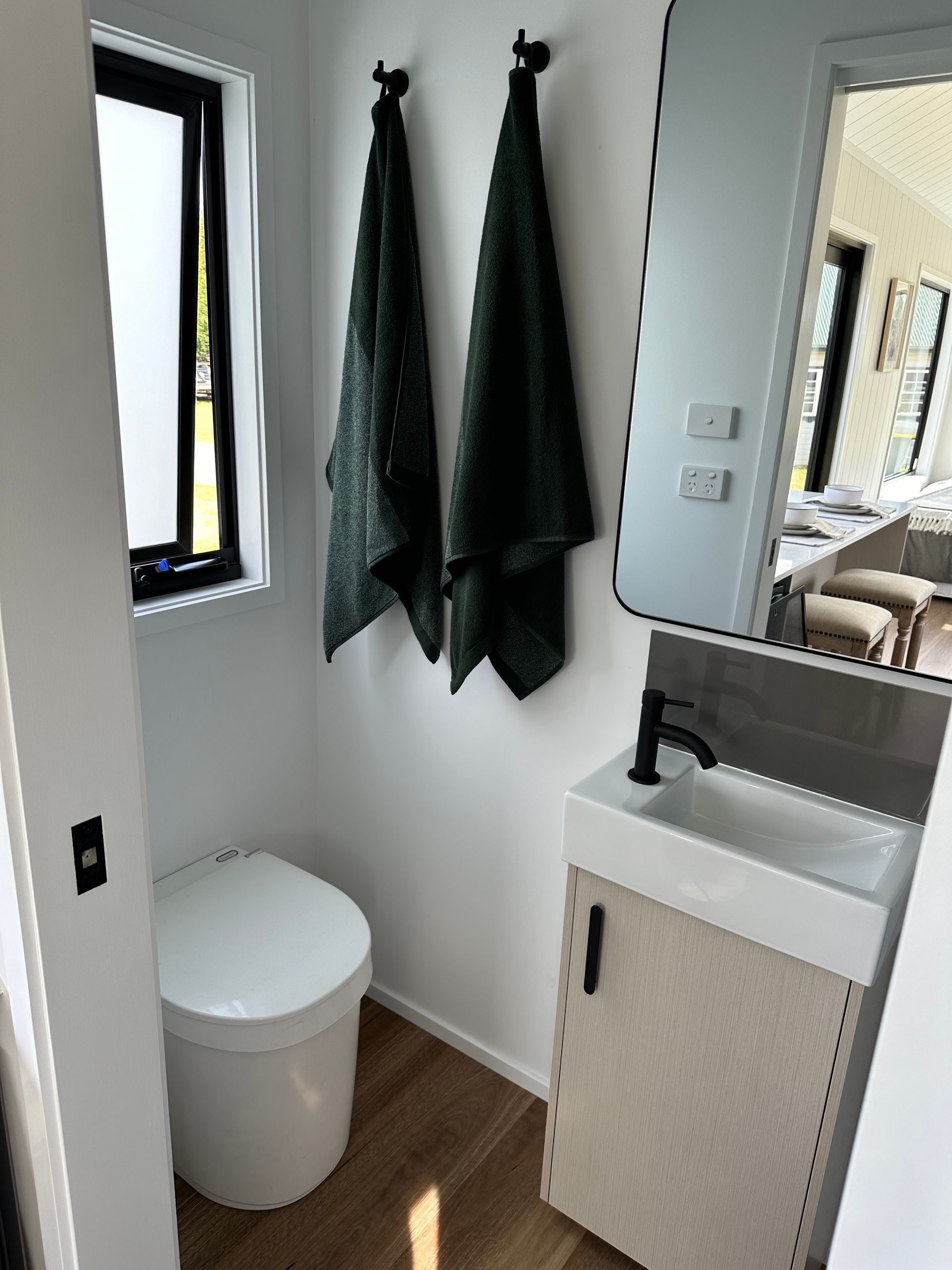 Small bathroom with toilet, sink, mirror, and towels hanging on wall.