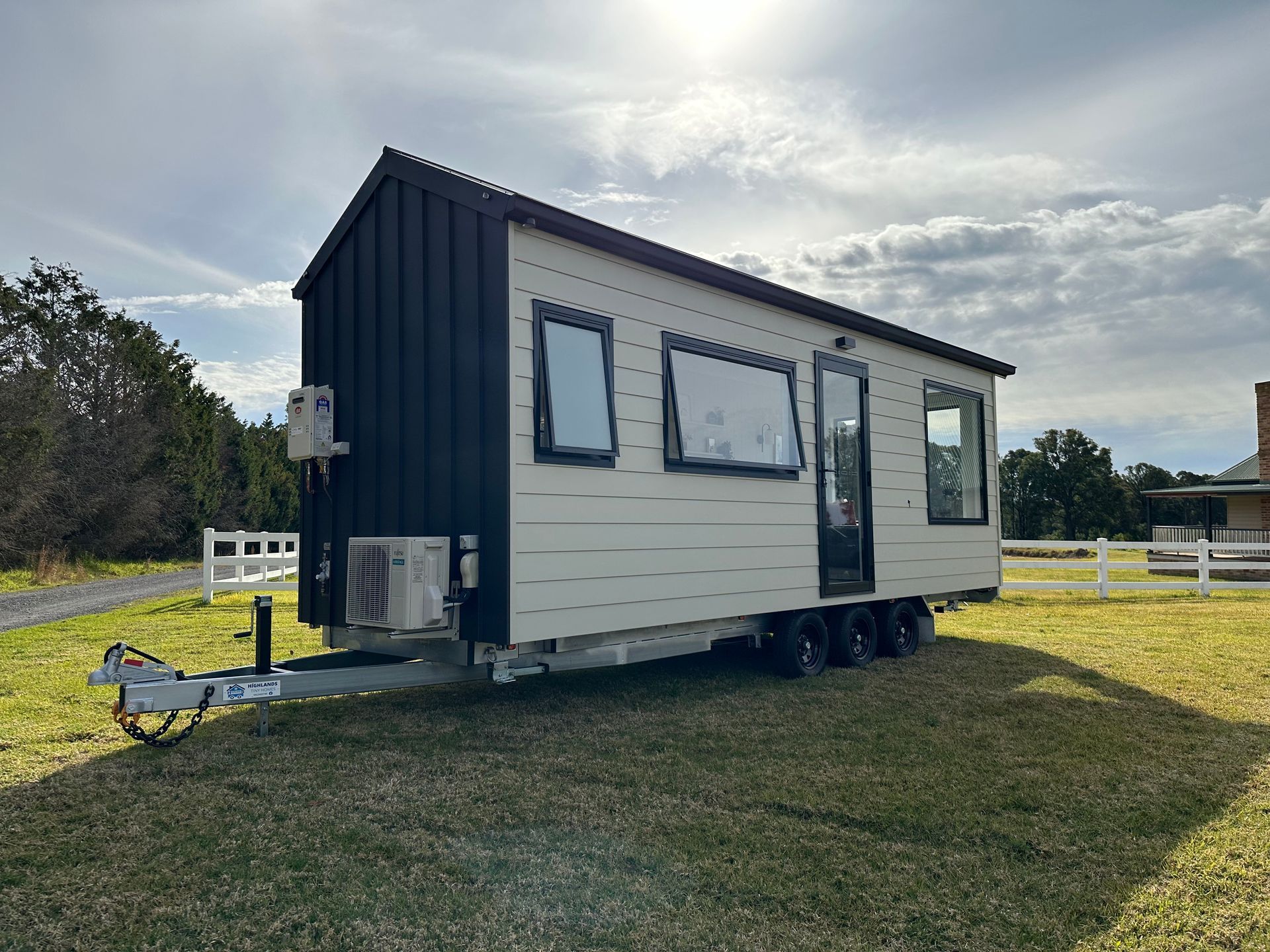 Tiny house on wheels, light exterior with dark accents, parked on grass field.