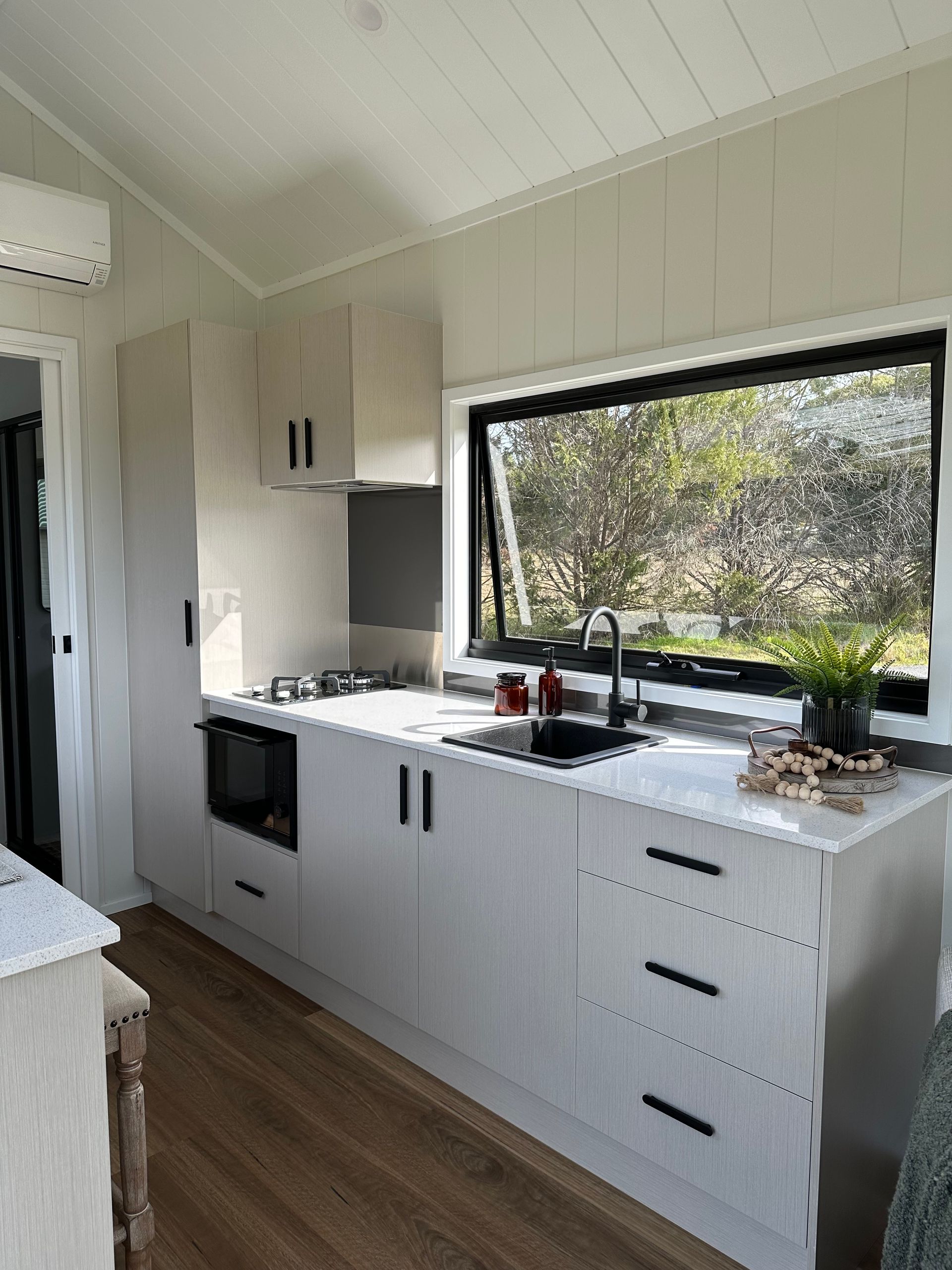 Small kitchen with white cabinets, black sink, window, and a microwave.