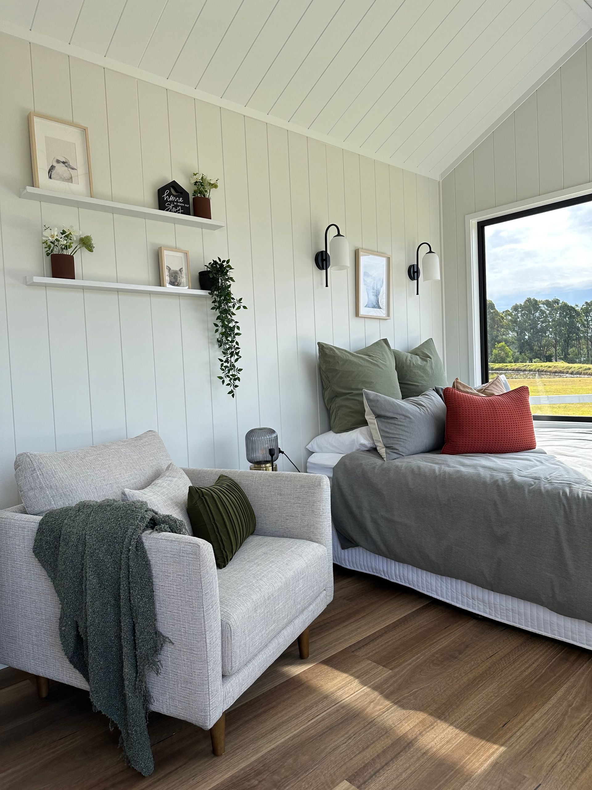 Cozy bedroom with accent wall, shelves, armchair, and bed near a window overlooking a field.