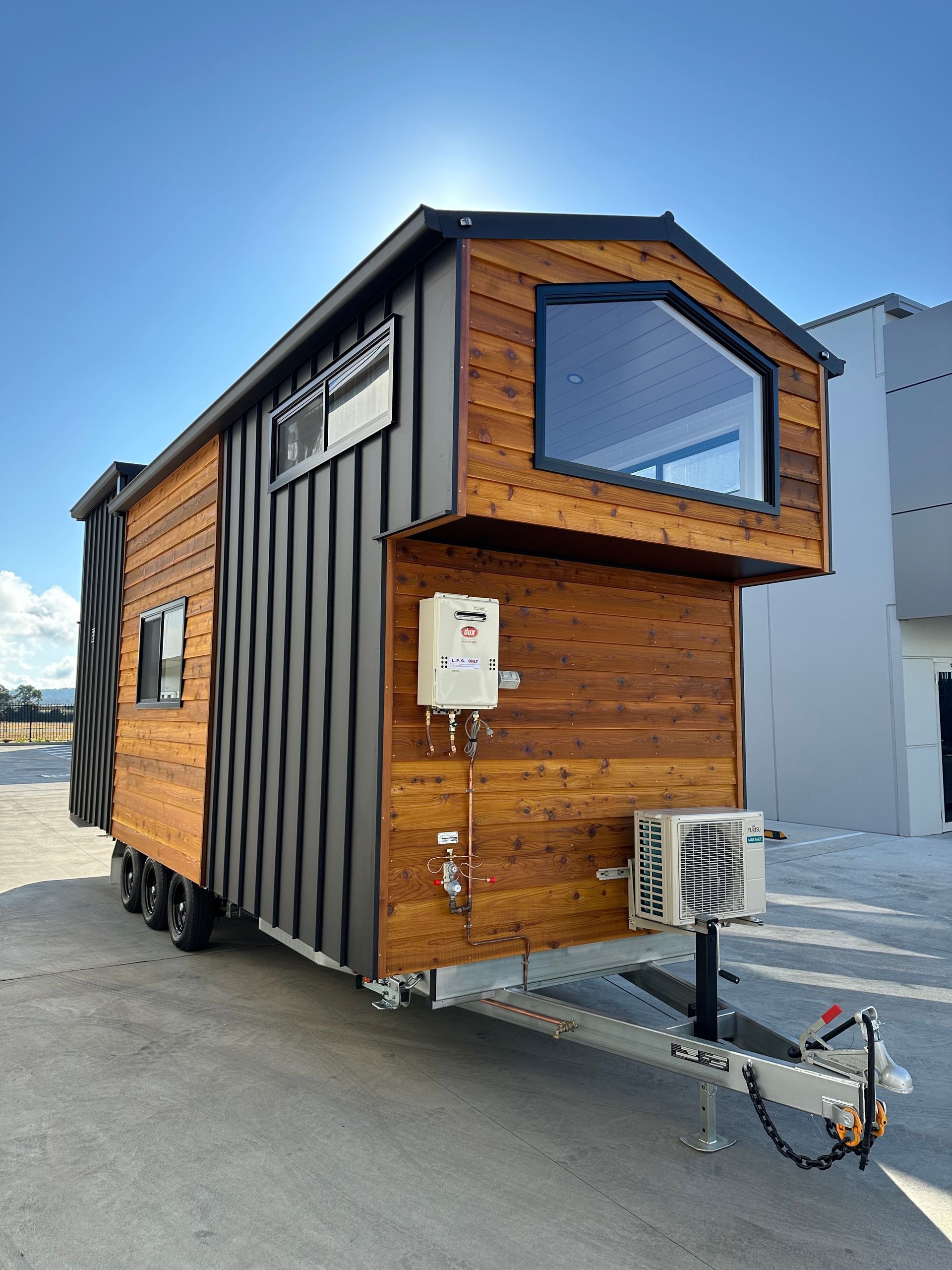 Tiny house on wheels with wood siding, black accents, and a large window against a blue sky.