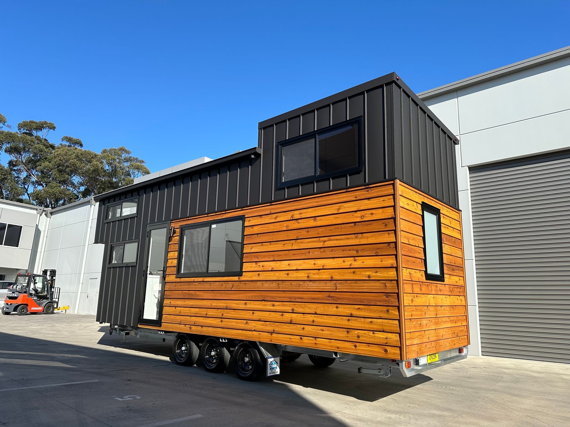 Tiny house on wheels with wood and black metal siding, parked outside.
