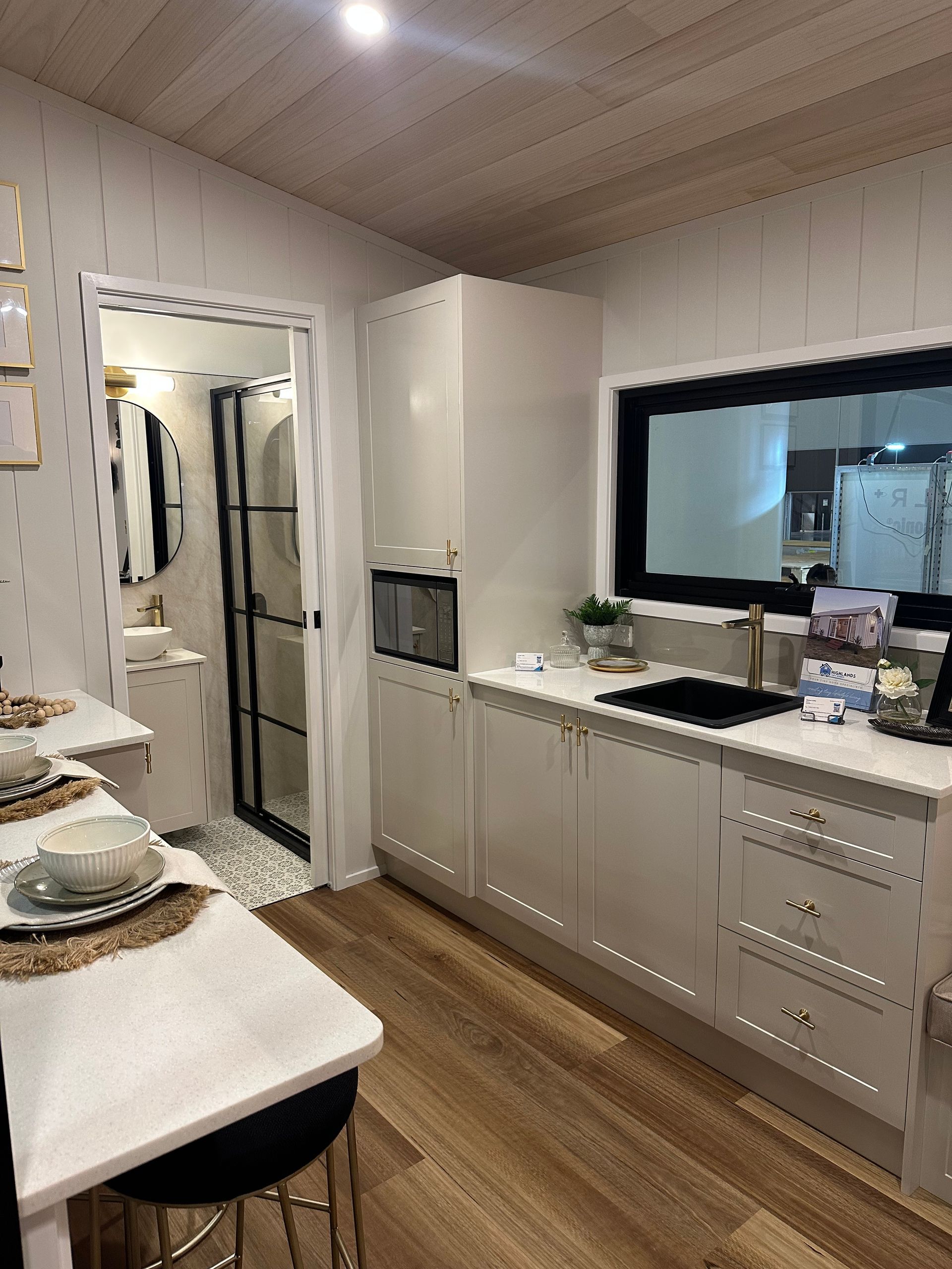 Interior of a tiny home with a bench seat, large window, and wooden ceiling.