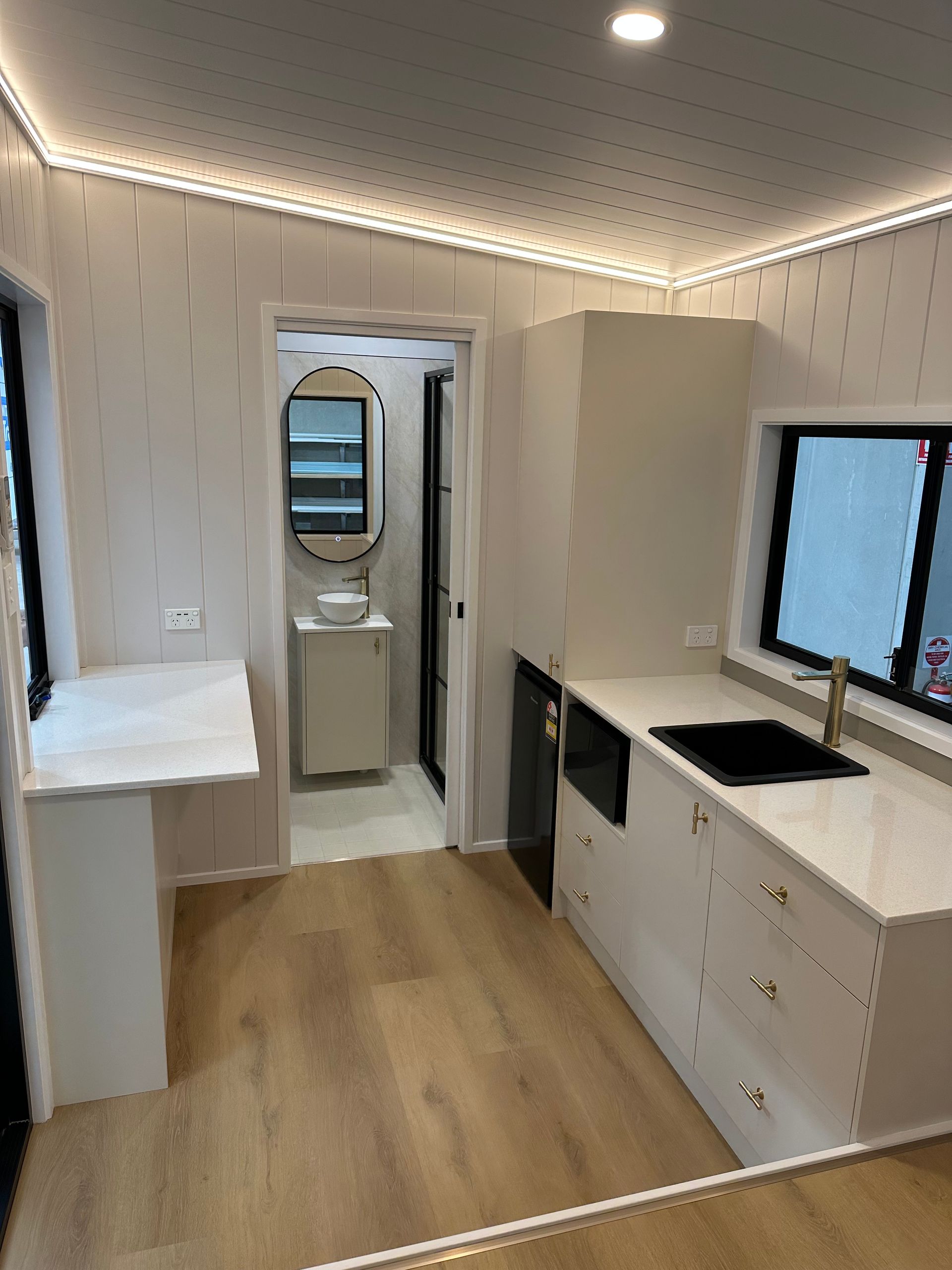 Interior view of a modern camper van, featuring a kitchen area with light wood floors, white cabinets, and a bathroom.