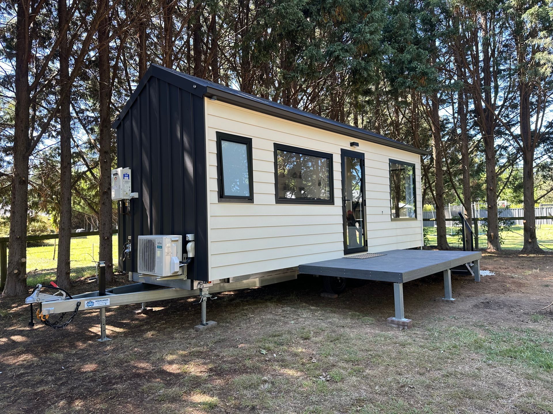 Dark gray tiny house on wheels with large windows and a side awning.