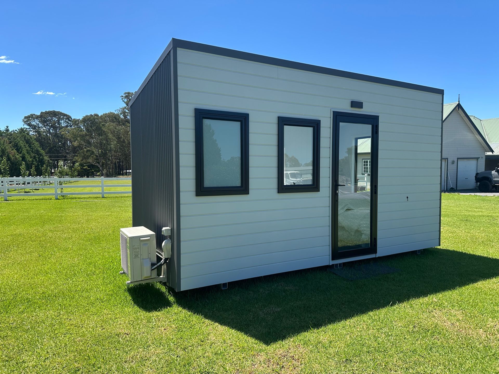 Small, modern, white cabin with black trim on a grassy lawn.