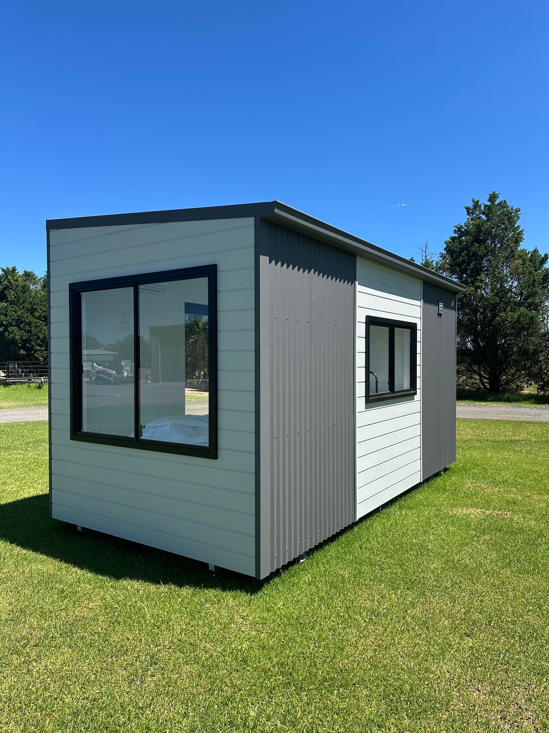 Tiny modern house with grey and white exterior, black window frames, on grassy lawn.
