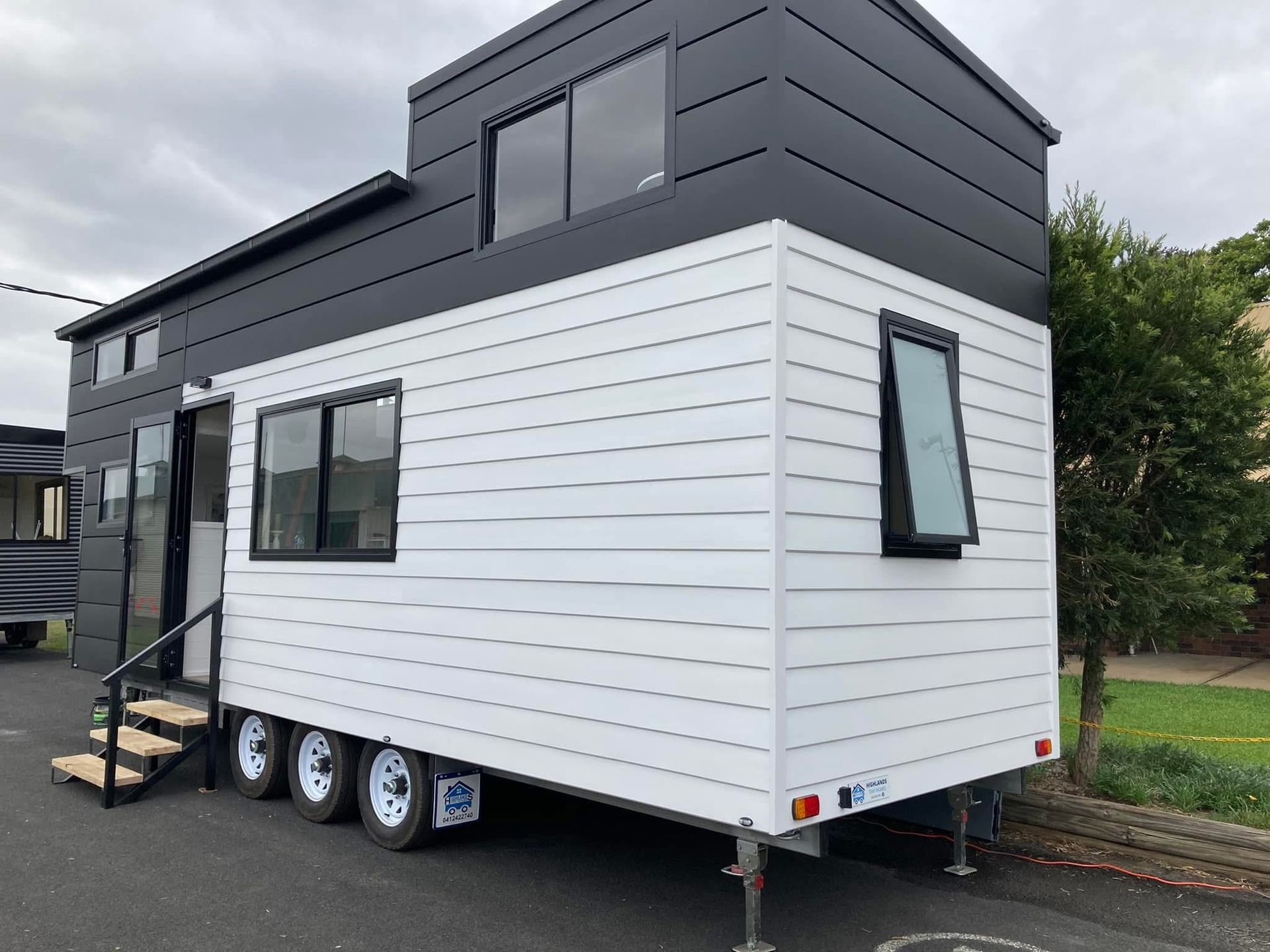 Tiny house on wheels with black and white siding, parked outdoors.