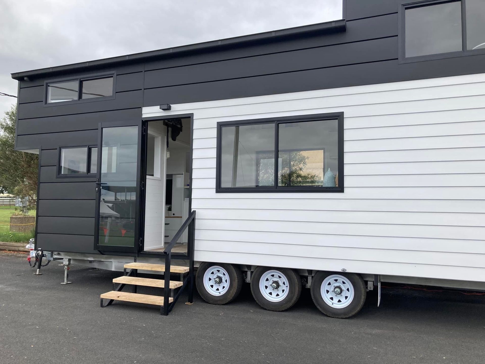 Tiny house trailer with black and white siding, windows, and steps.