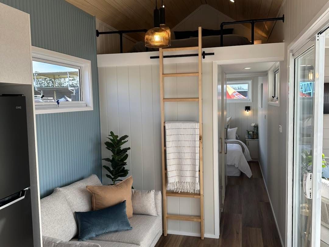 Cozy tiny home interior with a loft, sofa, ladder, and sliding glass door.