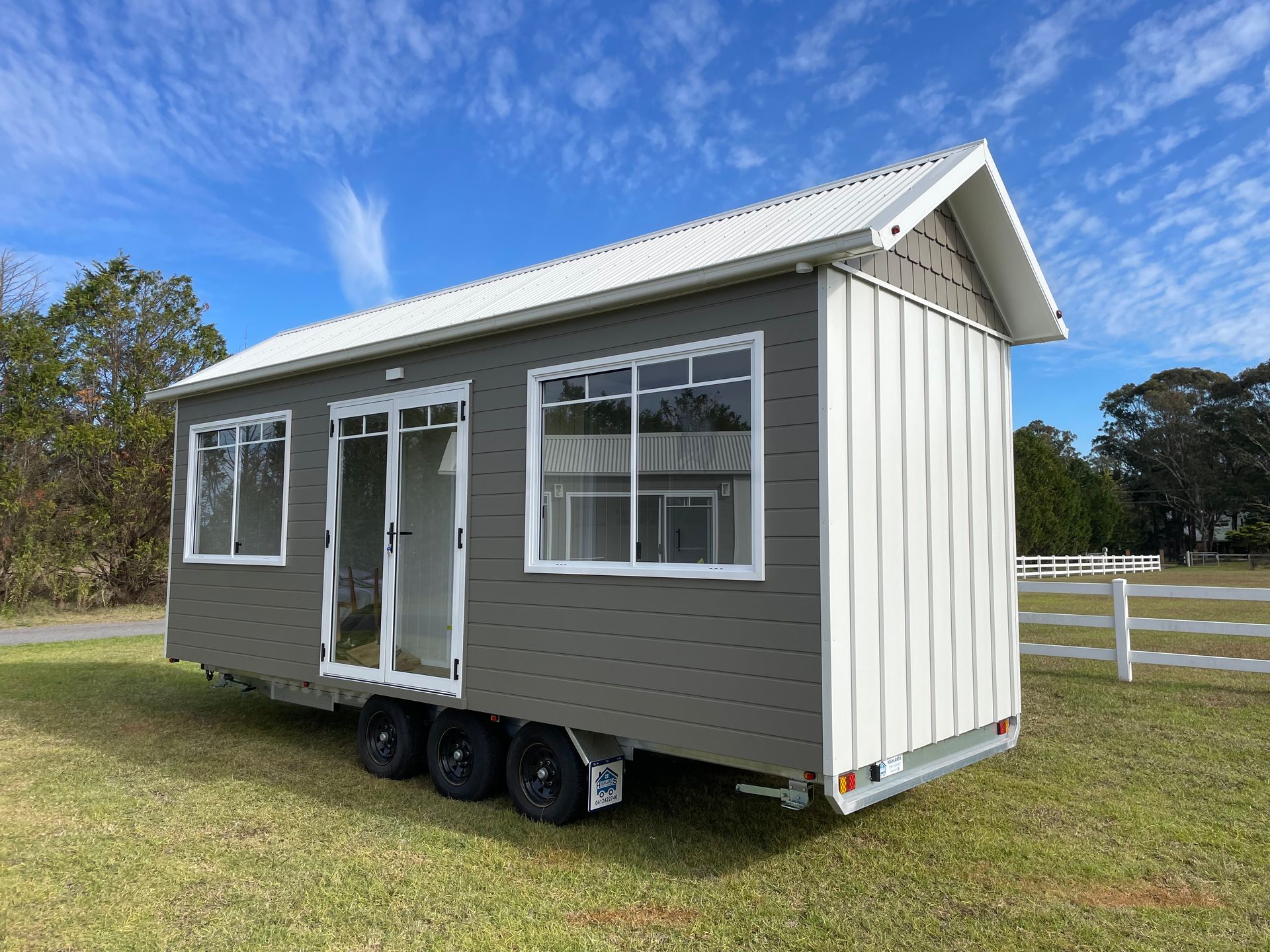 Tiny house on wheels, dark gray and beige siding, parked on concrete, overcast sky.