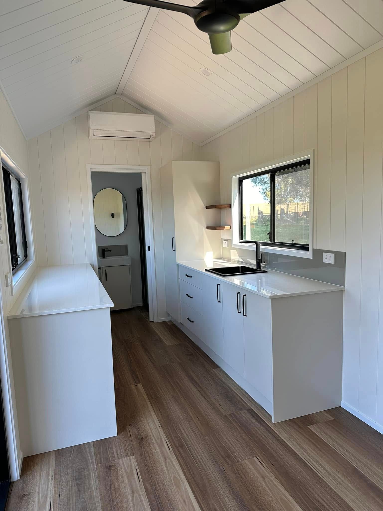 Interior view of a modern, bright kitchen and bathroom with white cabinetry and wood-look floors.