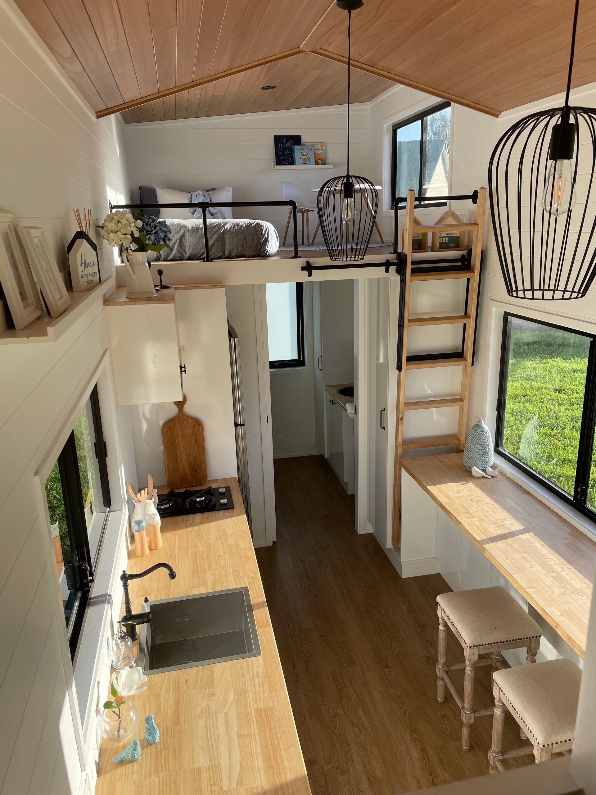 Tiny home interior with a loft bed, kitchen, and workspace.