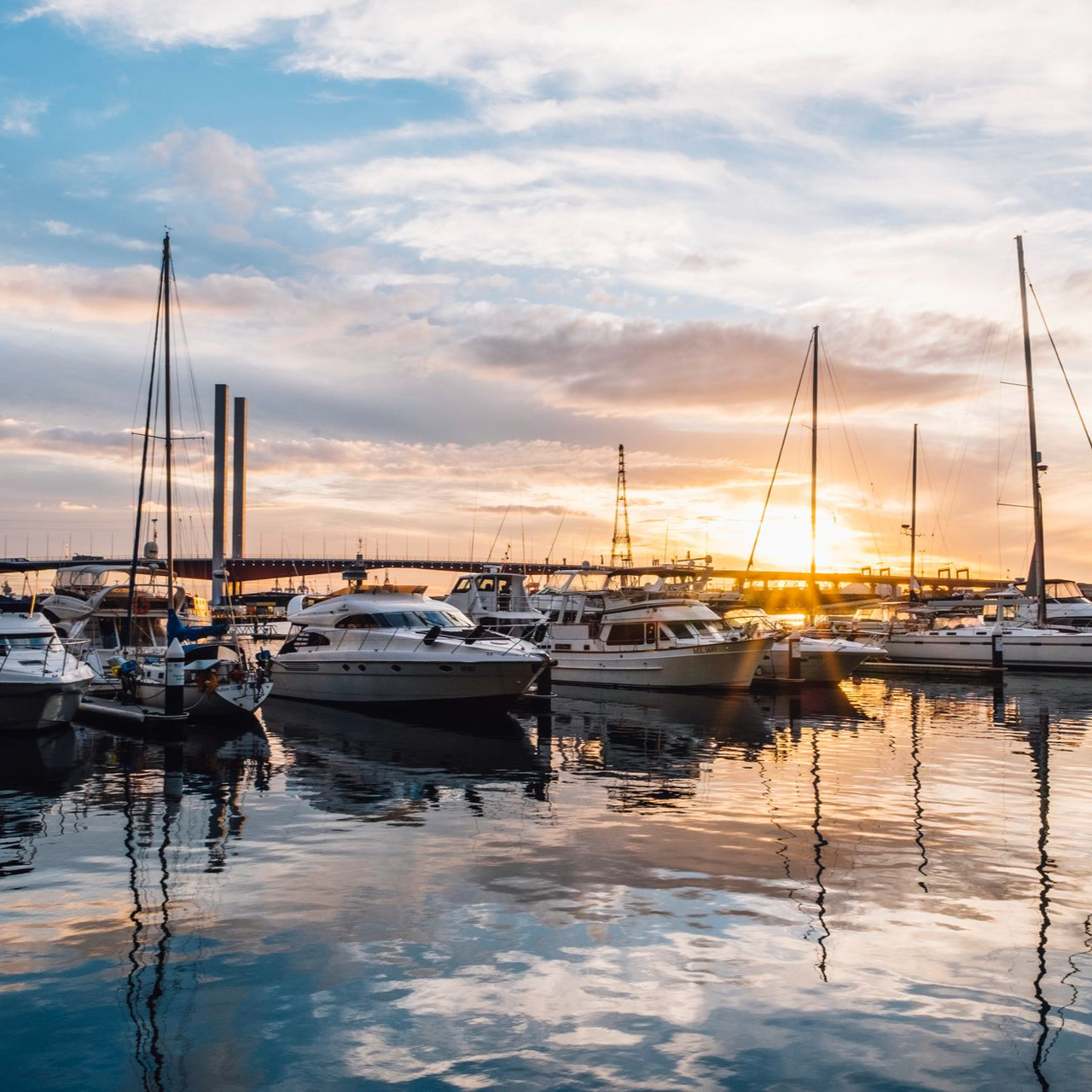 Sunset over a marina with sailboats and calm water reflecting the sky