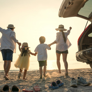 Family holding hands on a beach at sunset beside an open car trunk and shoes on the sand